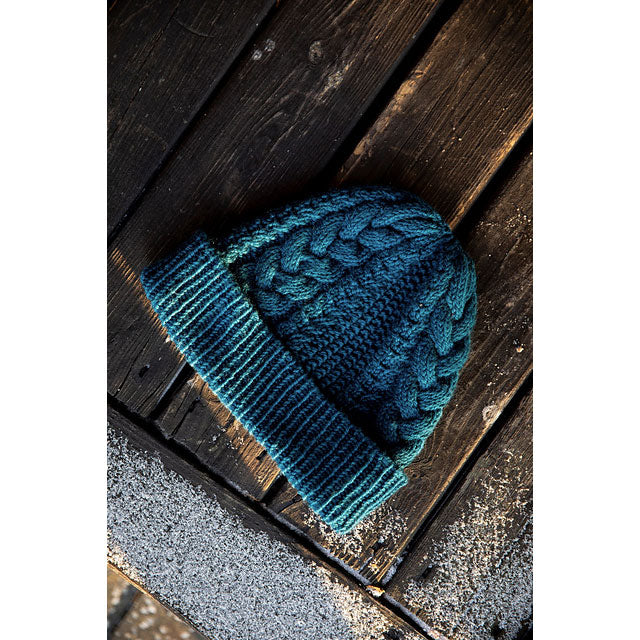 Dark blue cable textured knitted beanie hat with fold up ribbed brim lying on wooden decking