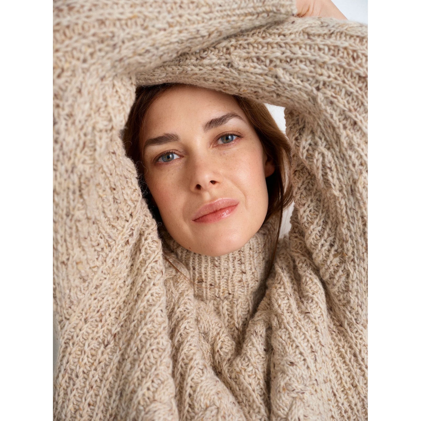Mooring by Meghan Babin. Woman wearing an oatmeal marled shade knitted sweater in fishermans rib with front cable panels