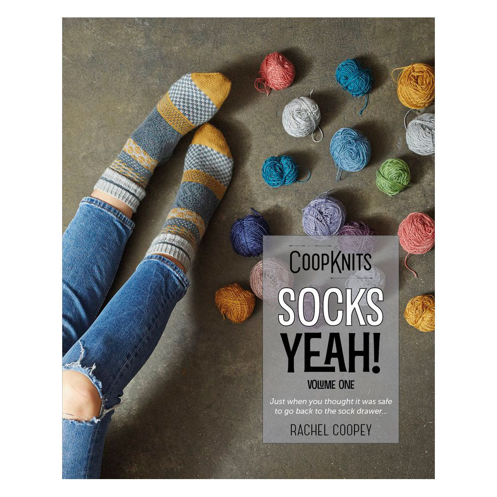 Book titled 'CoopKnits Socks Yeah! Volume One' by Rachel Coopey with striped socks and yarn balls on a textured surface.