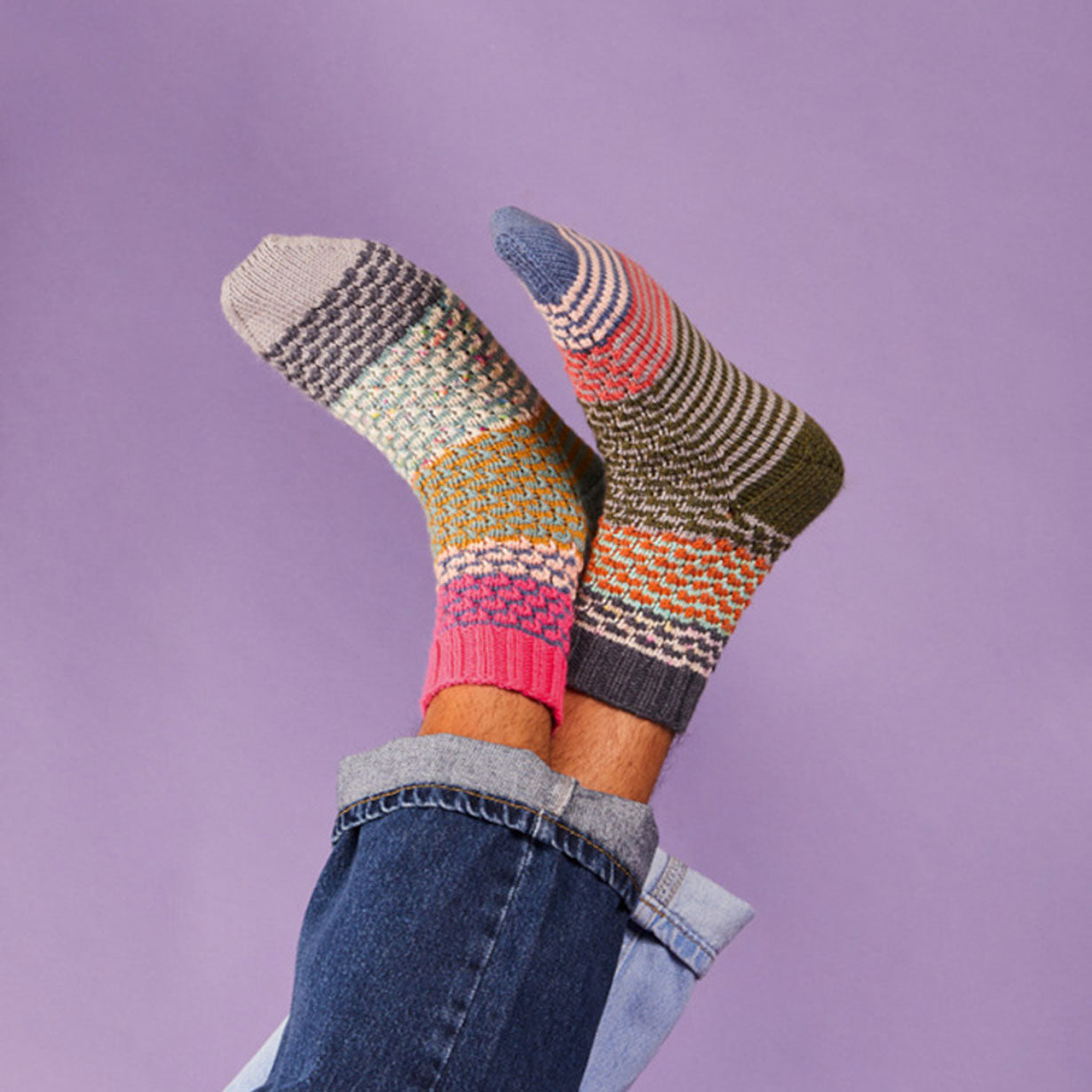 Colorful patterned socks worn with jeans against a purple background