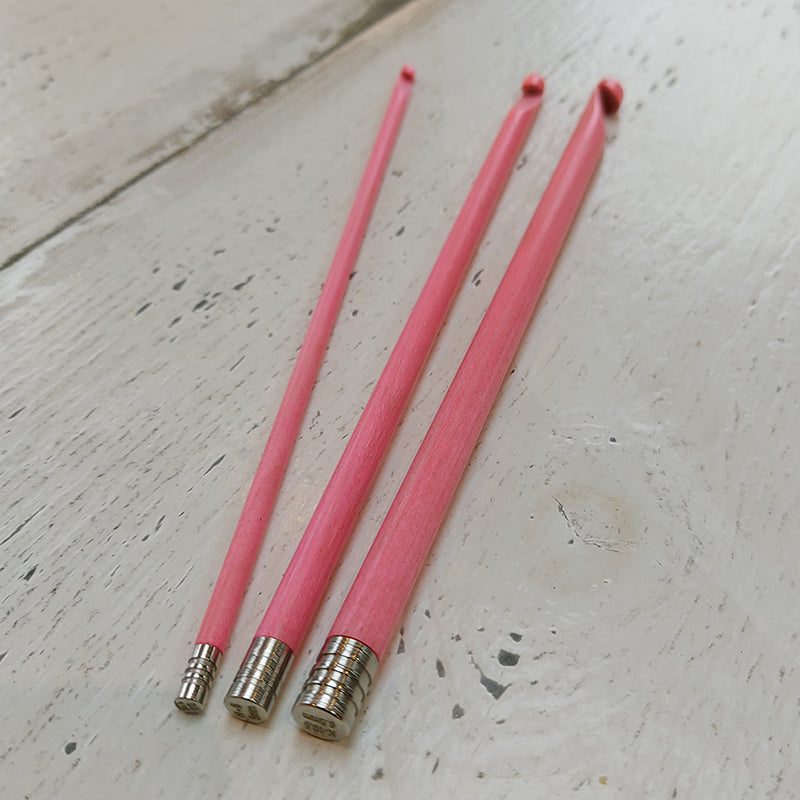 Trio of LYKKE blush pink crochet hooks with silver coloured finials on a pale white wooden surface