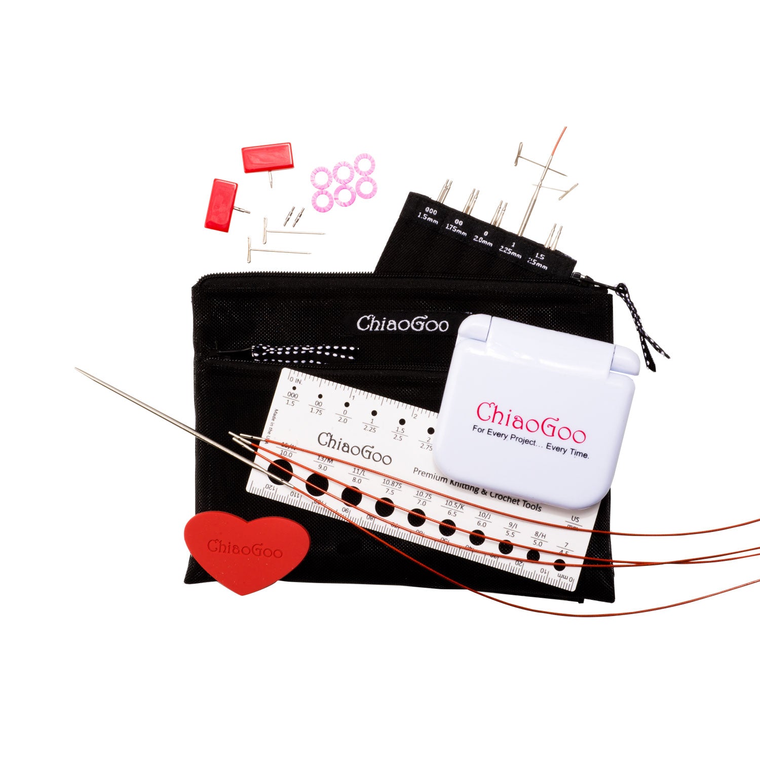 ChiaoGoo 4in Mini set showing labelled tip sleeve with screw ends of tips showing and tightening keys in one tip and cable, three red lace cables lying flat, a white plastic ruler needle gauge and white plastic click shut container with red ChiaoGoo logo, red rubber heart, two red mini end stoppers, six pink stitch markers, two MINI T-pins and two MINI cable connectors