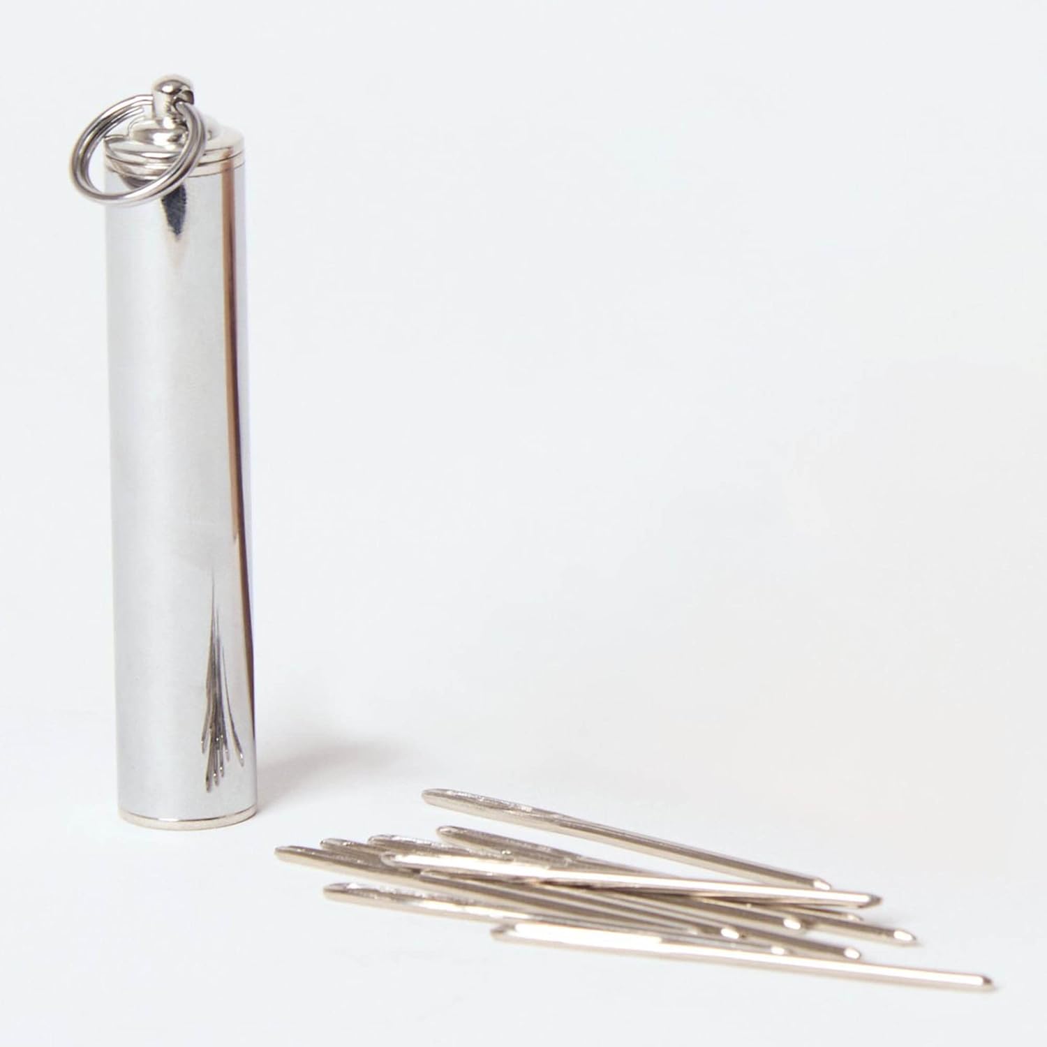 Silver coloured cylinder with darning needles in a small pile to the side on a white background