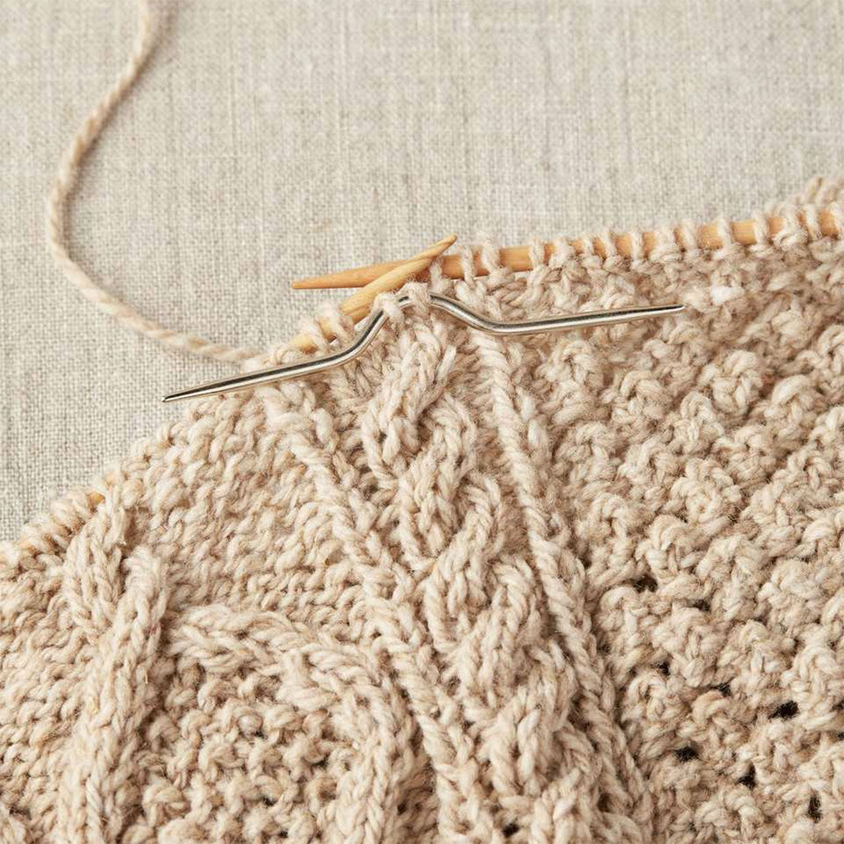 Close-up of knitting needles and stainless steel curved cable in use on beige knitting on linen background