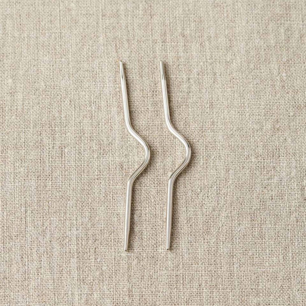 Pair of stainless steel curved cabele needles on linen background