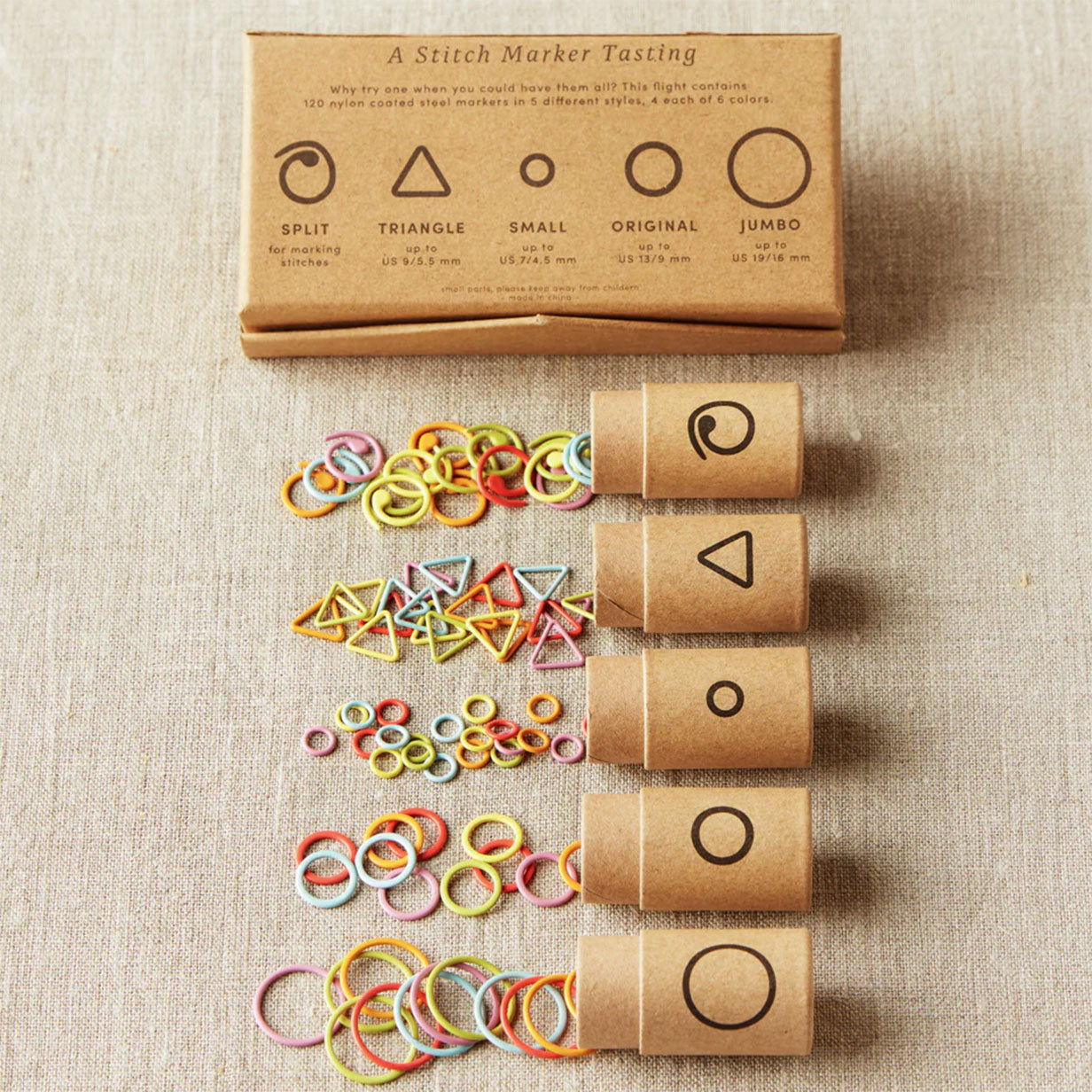 Set of colourful stitch markers with packaging on a beige fabric background