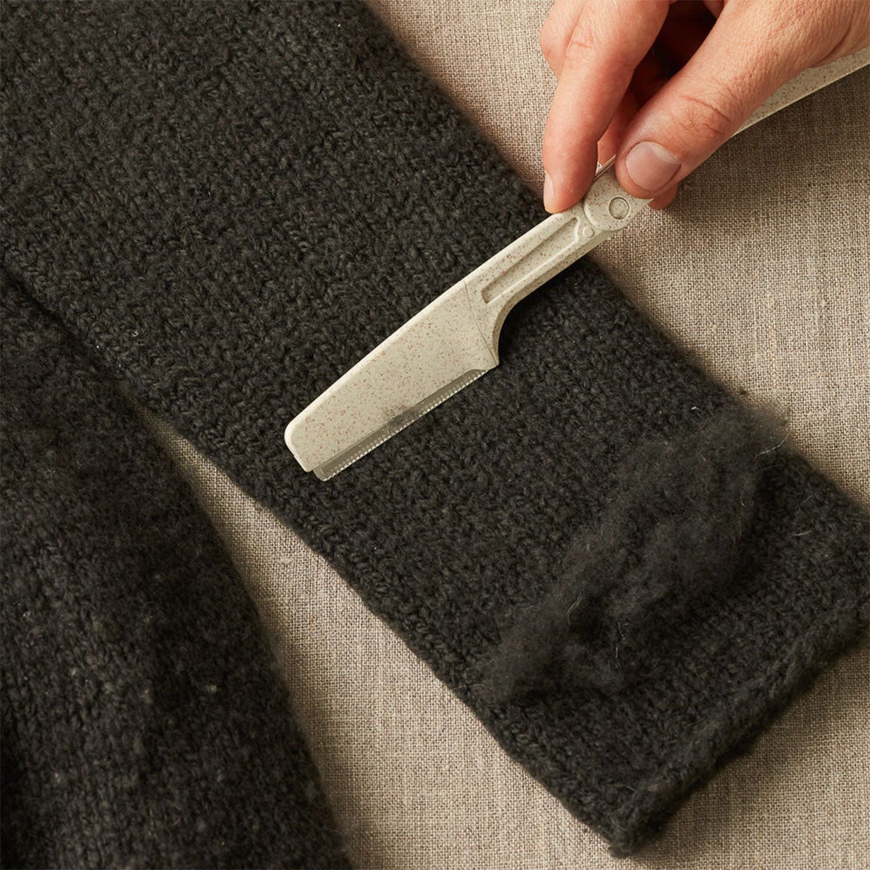 Person using the Cocoknits defuzzer tool on a dark knitted surface