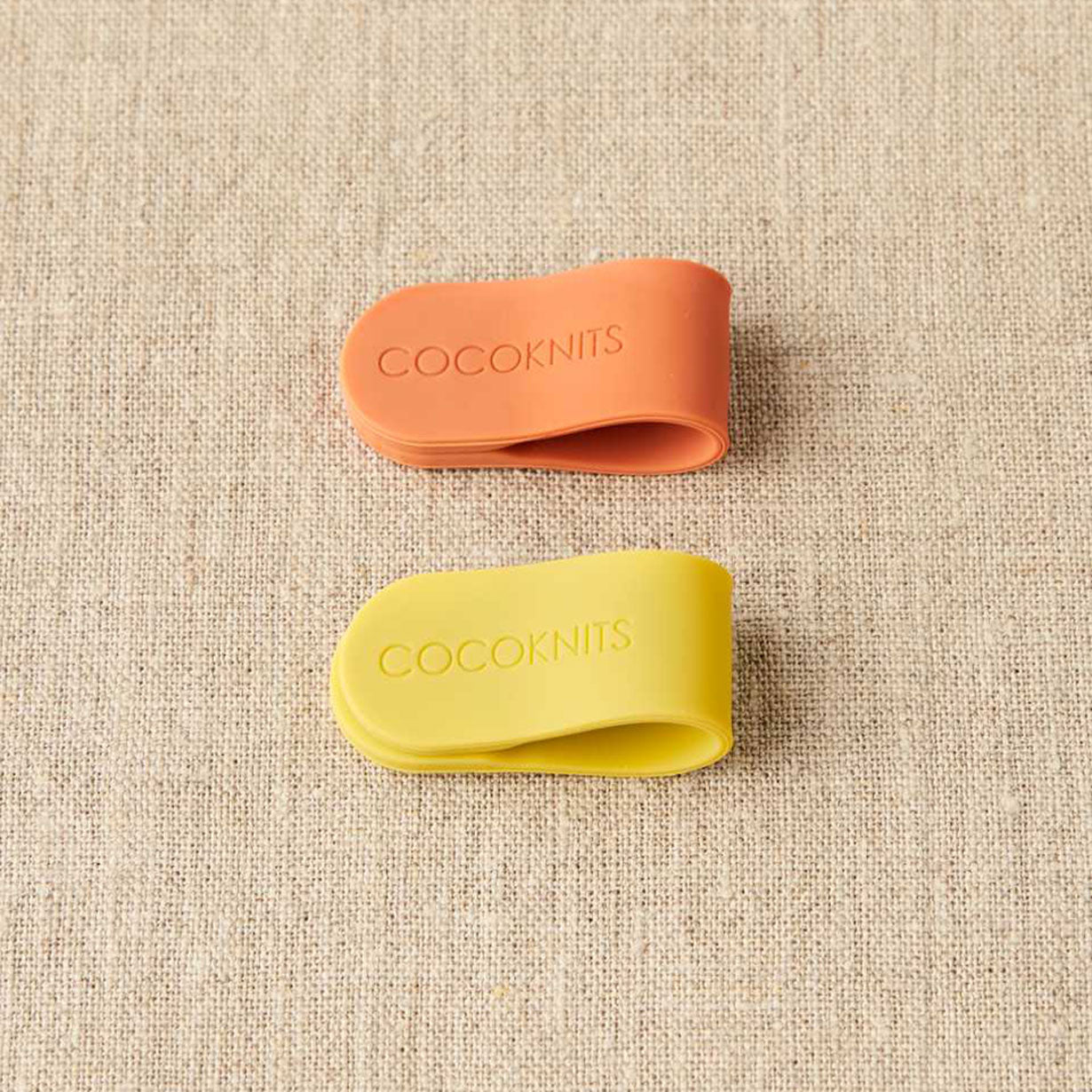 Cocoknits magnetic clips, one brick orange, one yellow on linen background