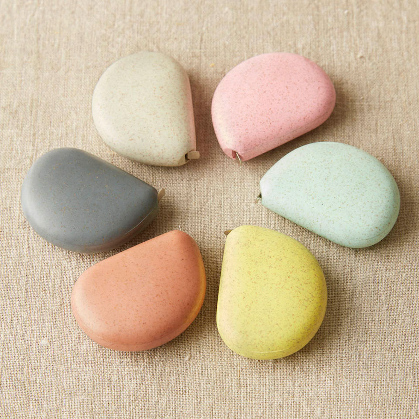 Six pebble shaped tape measures in pastel colours on a linen background