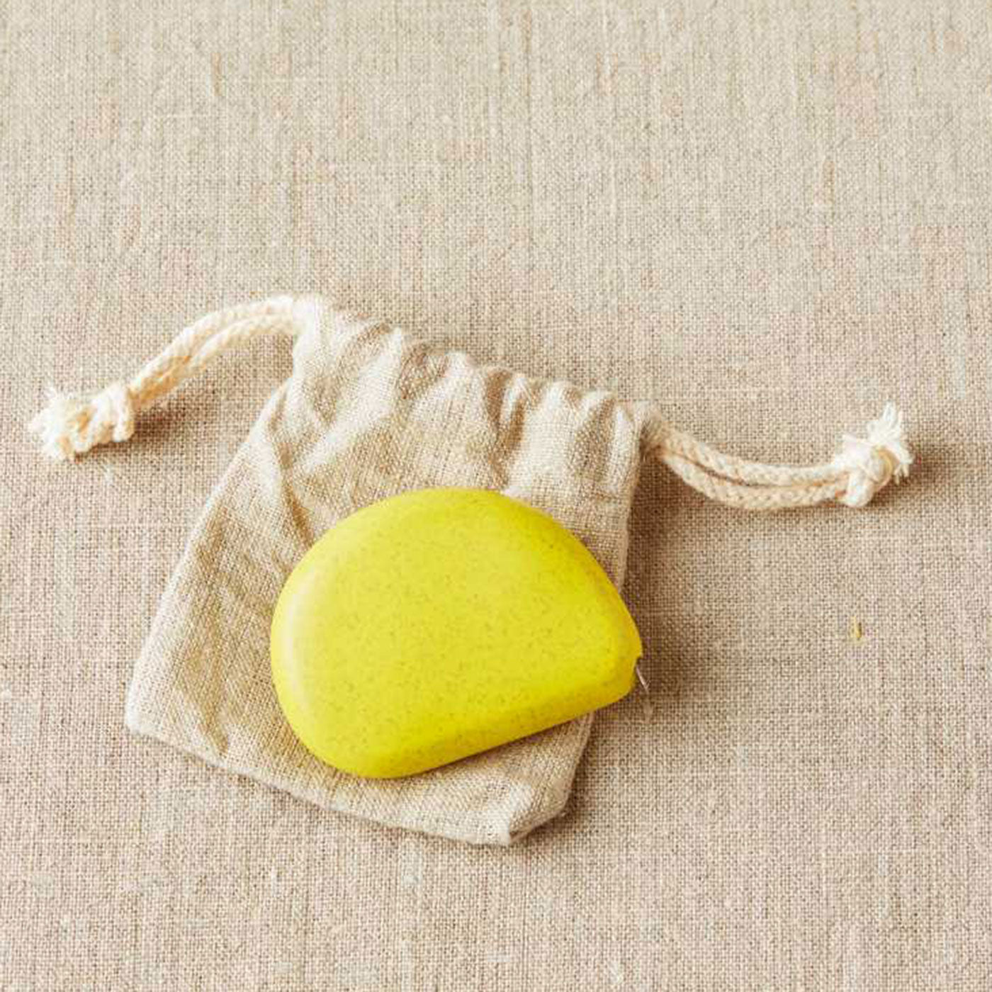 Yellow coloured pebble shaped tape measure on linen drawstring bag