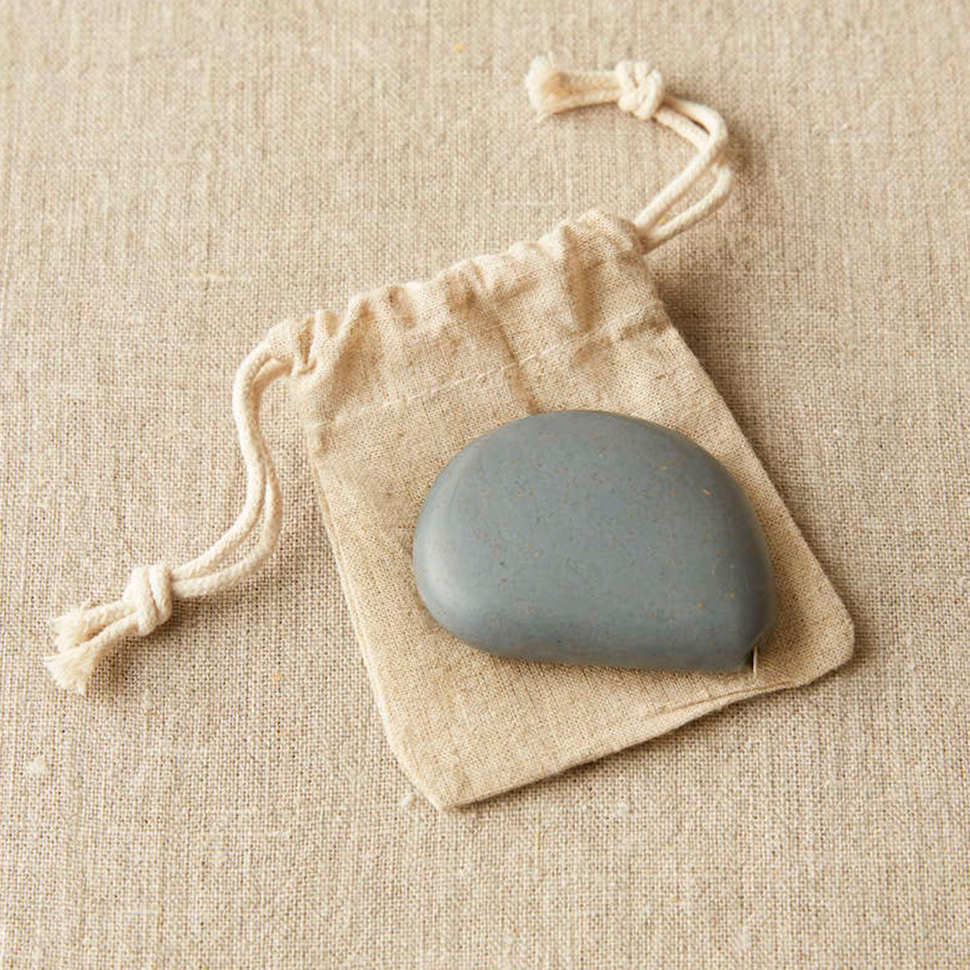 Dark grey coloured pebble shaped tape measure on linen drawstring bag