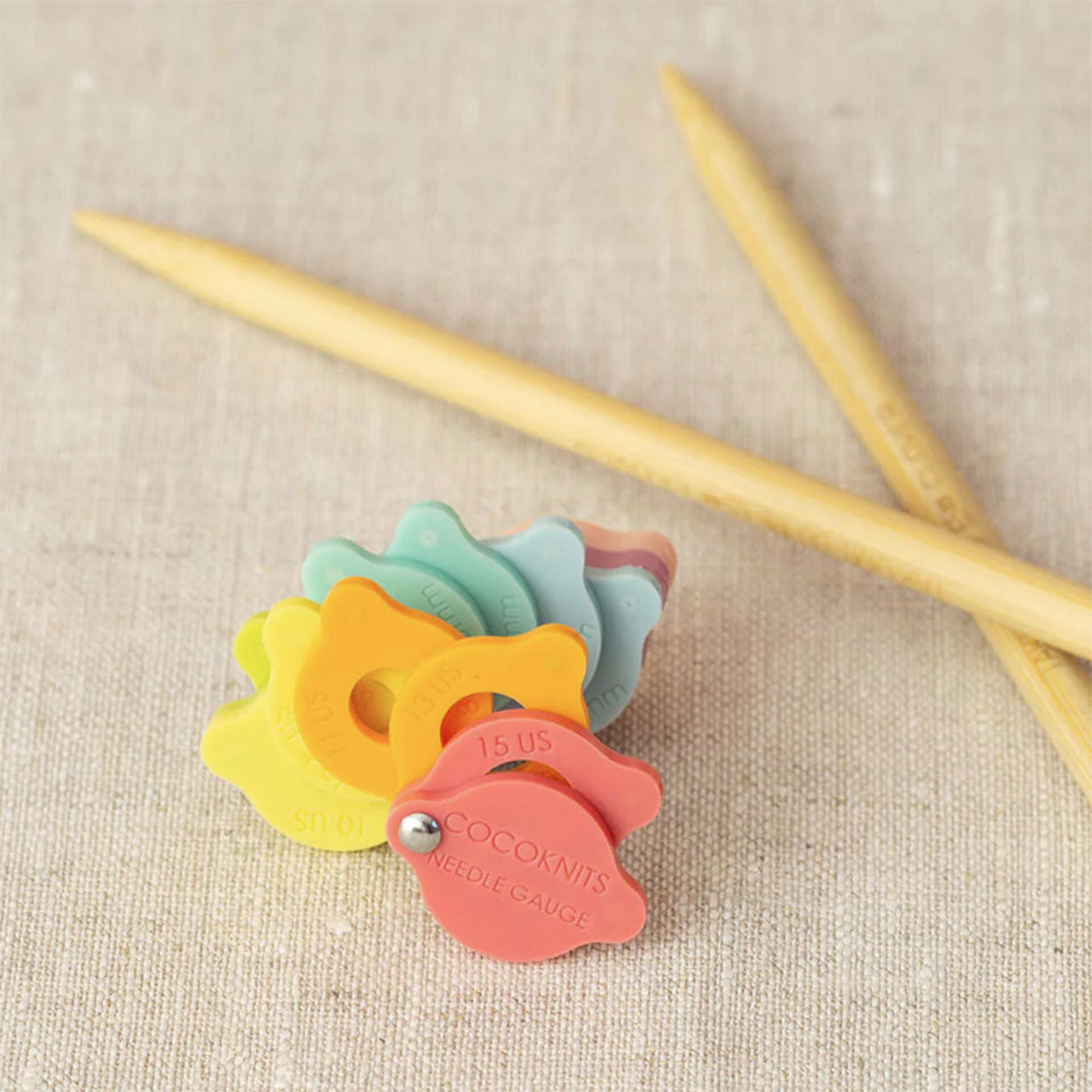 Crossed pair of knitting needles behind fanned shape of needle sizer gauge