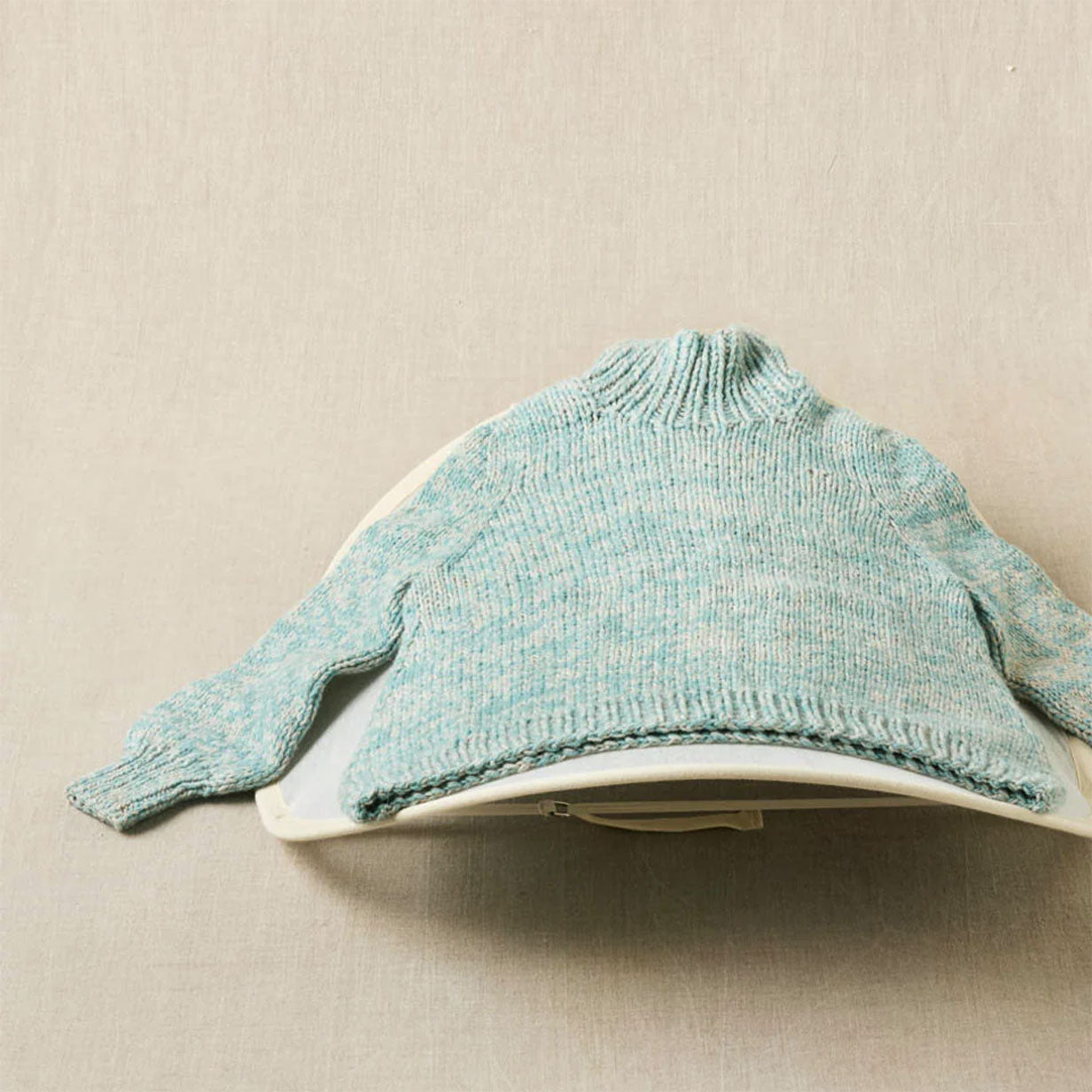 Teal knitted sweater drying on a sweater dryer placed on a linen background