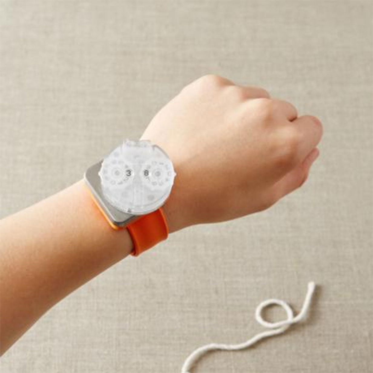 Persons wrist wearing an orange Cocoknits magnetic Makers Keep with the premium row counter attached on the magnetic "face"