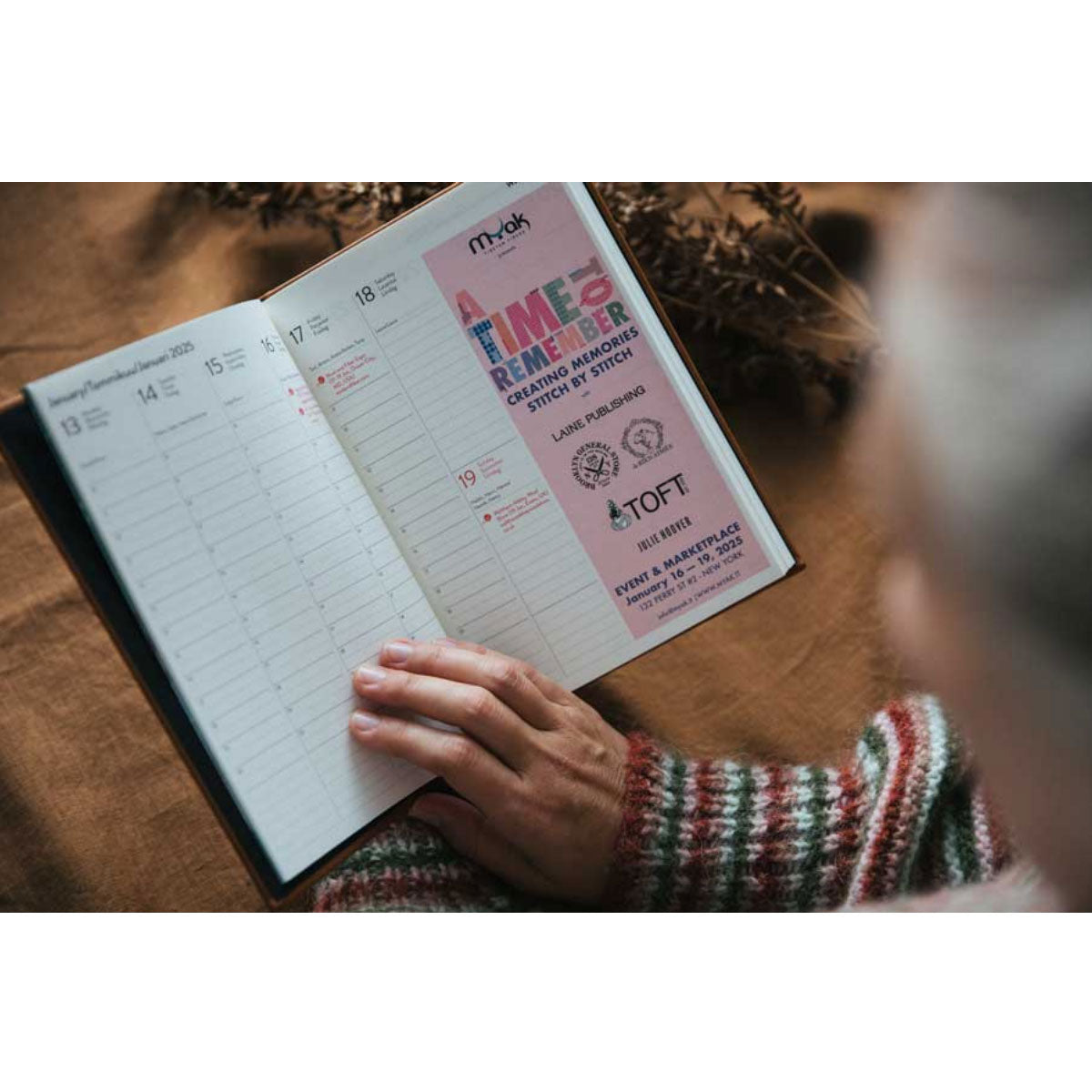 Person holding a planner with a pink flyer on a wooden surface