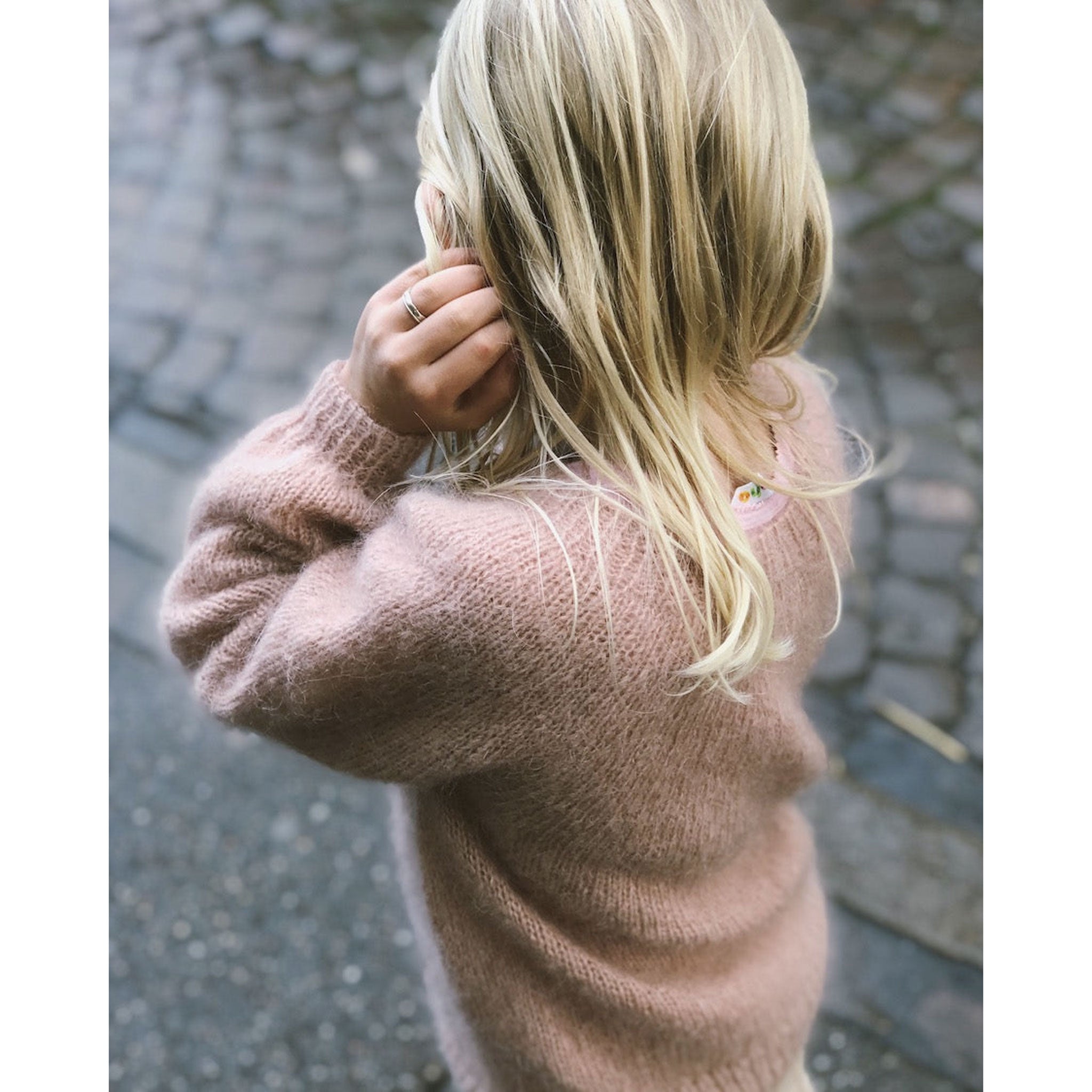 Young person wearing a knitted pink sweater with a blurred background