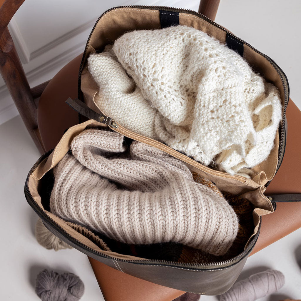 Interior of dark green leather knitting project bag showing knitting projects, the ecru coloured cotton lining and central divider with zipped closure
