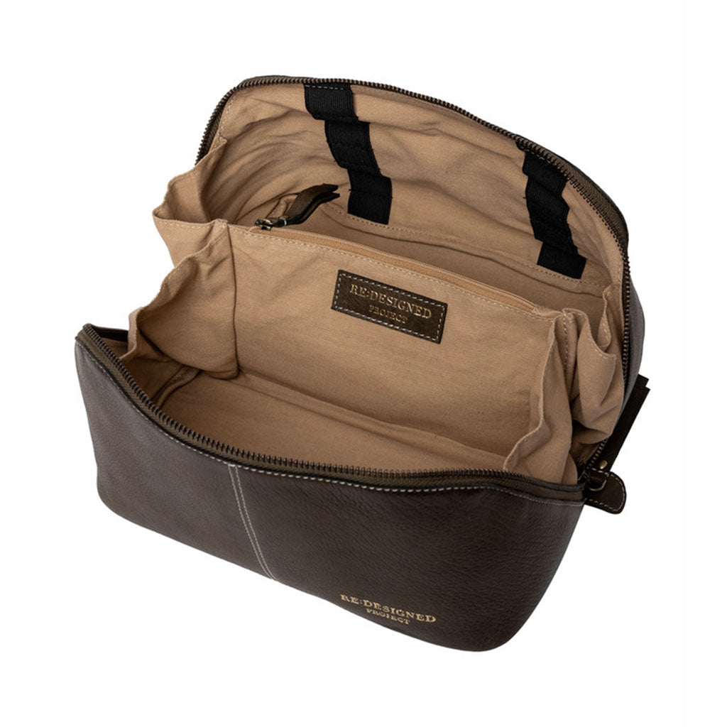 View of ecru coloured cotton lining interior of dark green leather knitting project bag, showing elastic strapping on one side for hooks, short needles, tips or DPNs, central dividing panel with zip closure, placed on a white surface