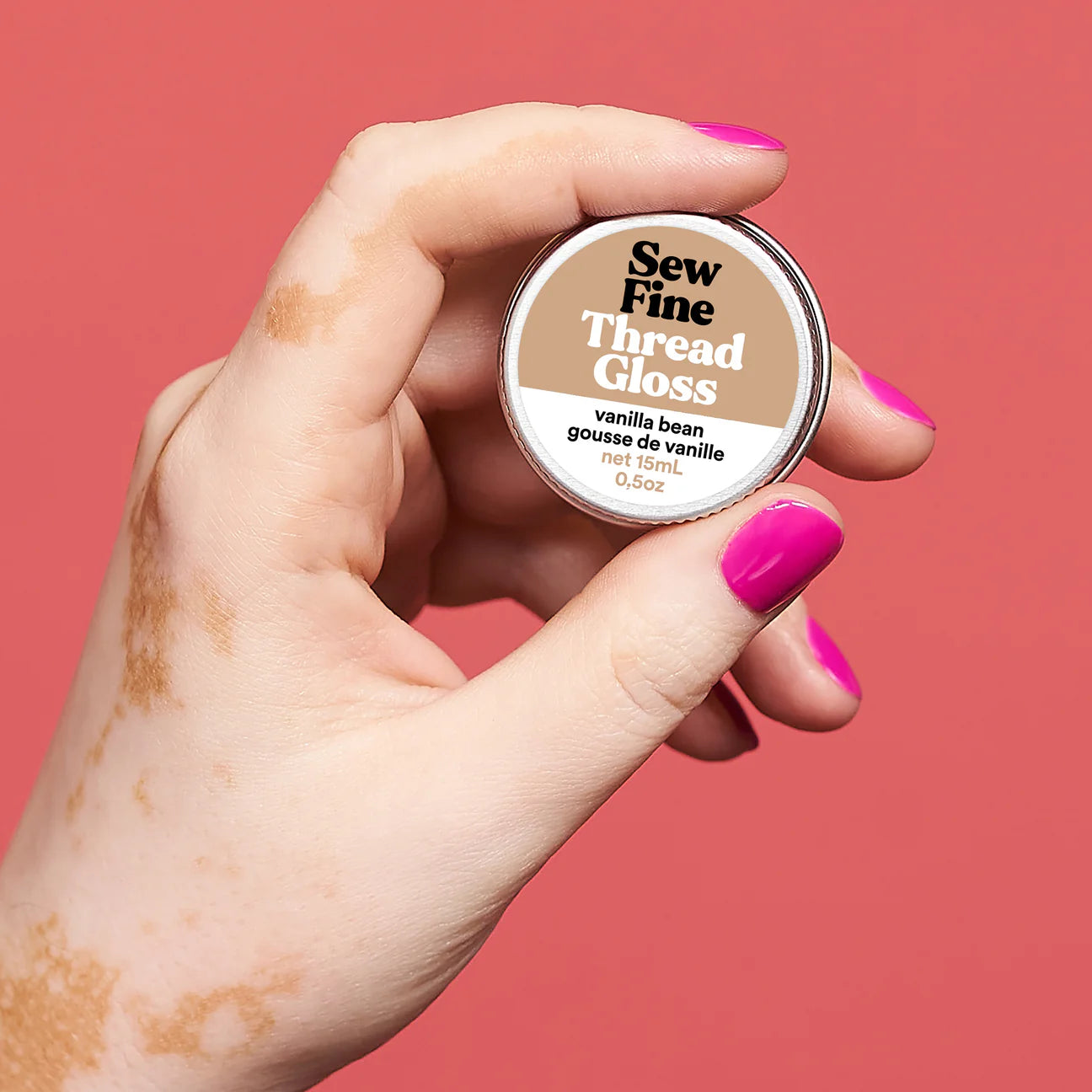 Hand holding a labelled tin of Sew Fine coral colour background