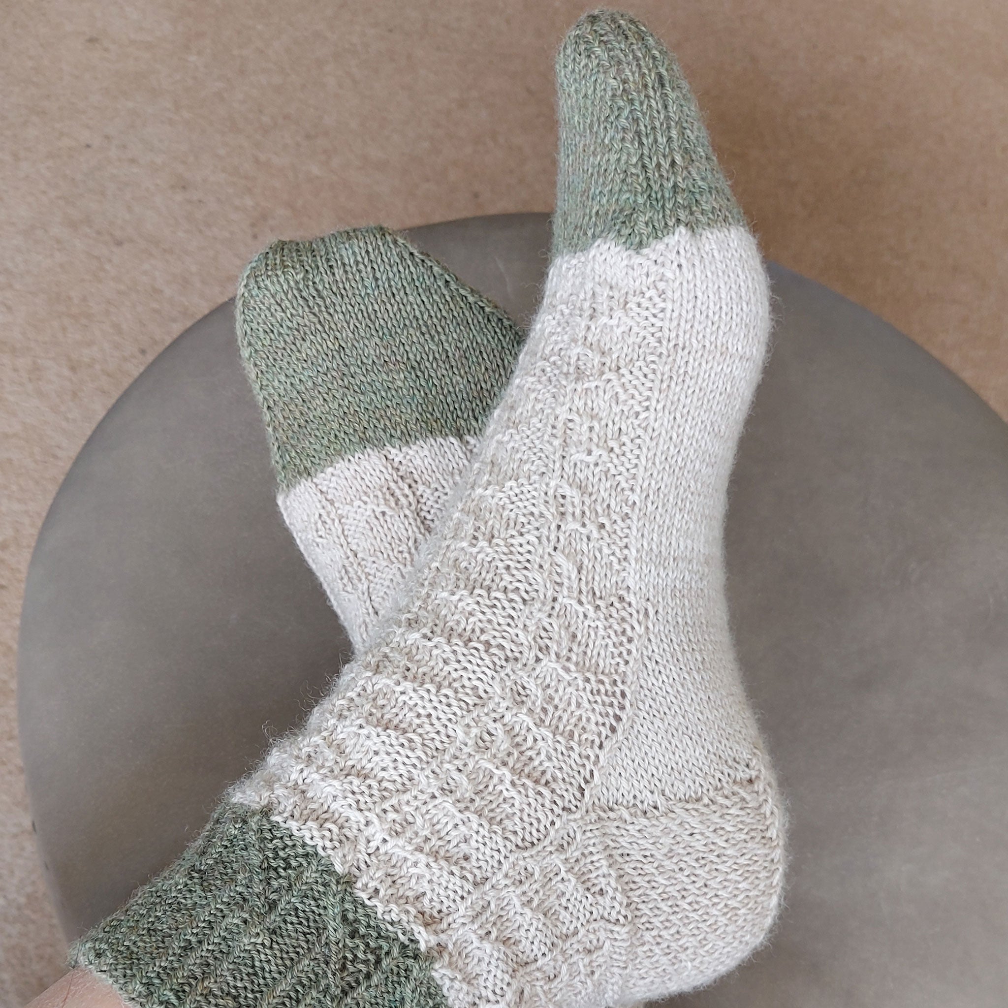 Pair of knitted socks being worn feet crossed, pattern Shirley from Socks Yeah! Book One, shades quartz and aventurine