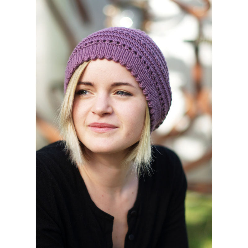 Person wearing purple coloured knitted slouch hat with picot rim, garter stitch contrast and eyelets