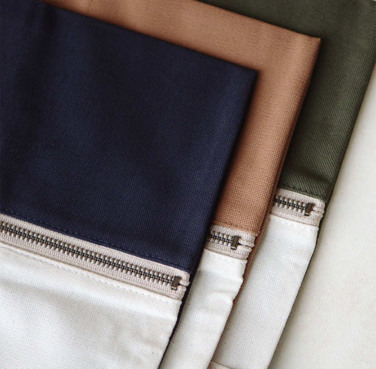 Close-up of folded fabric in navy blue, camel brown and olive green with a zipper detail.