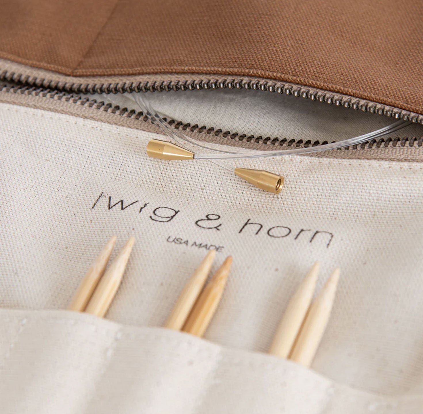 Interior of camel canvas interchangeable knitting needle case showing Twig & Horn logo, zipper, a coiled nylon interchangeable cable with brass connectors and bamboo tips on display