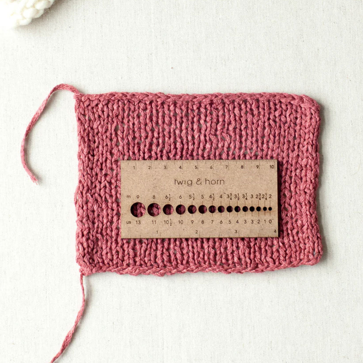 Twig & Horn MDF small ruler gauge placed on sample of pink stocking stitch