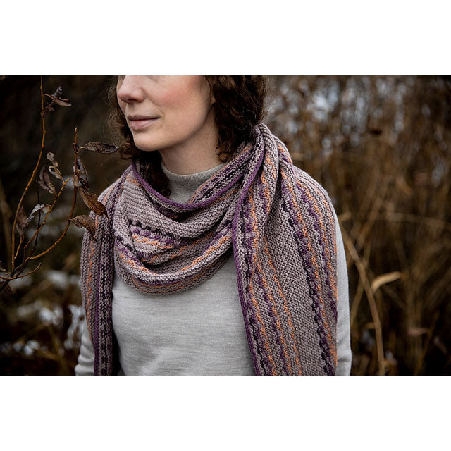 Person wearing a patterned scarf in a natural setting with snow and plants.
