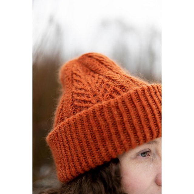 Close-up of a person wearing an orange knit beanie with a blurred natural background