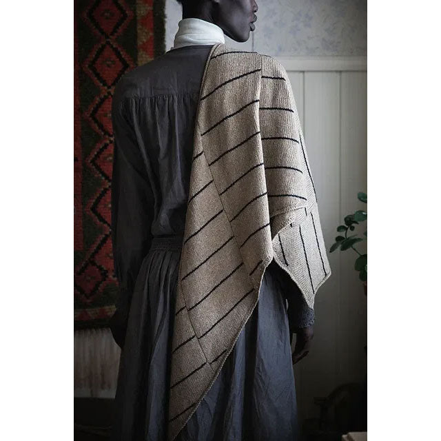  Ruf by Aude Martin Person wearing a beige and black knitted striped shawl in a room with patterned wall and plant.