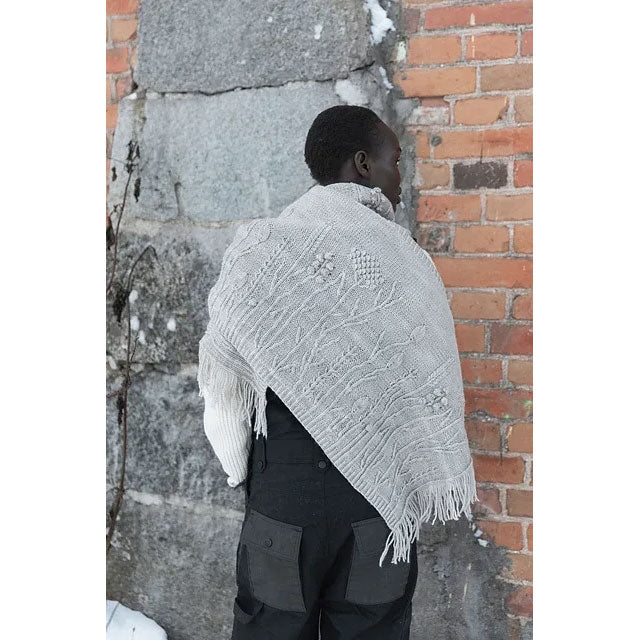 Wild Flowers by Katya Gorbacheva. Person wearing a light gray knitted shawl against a stone and brick wall.