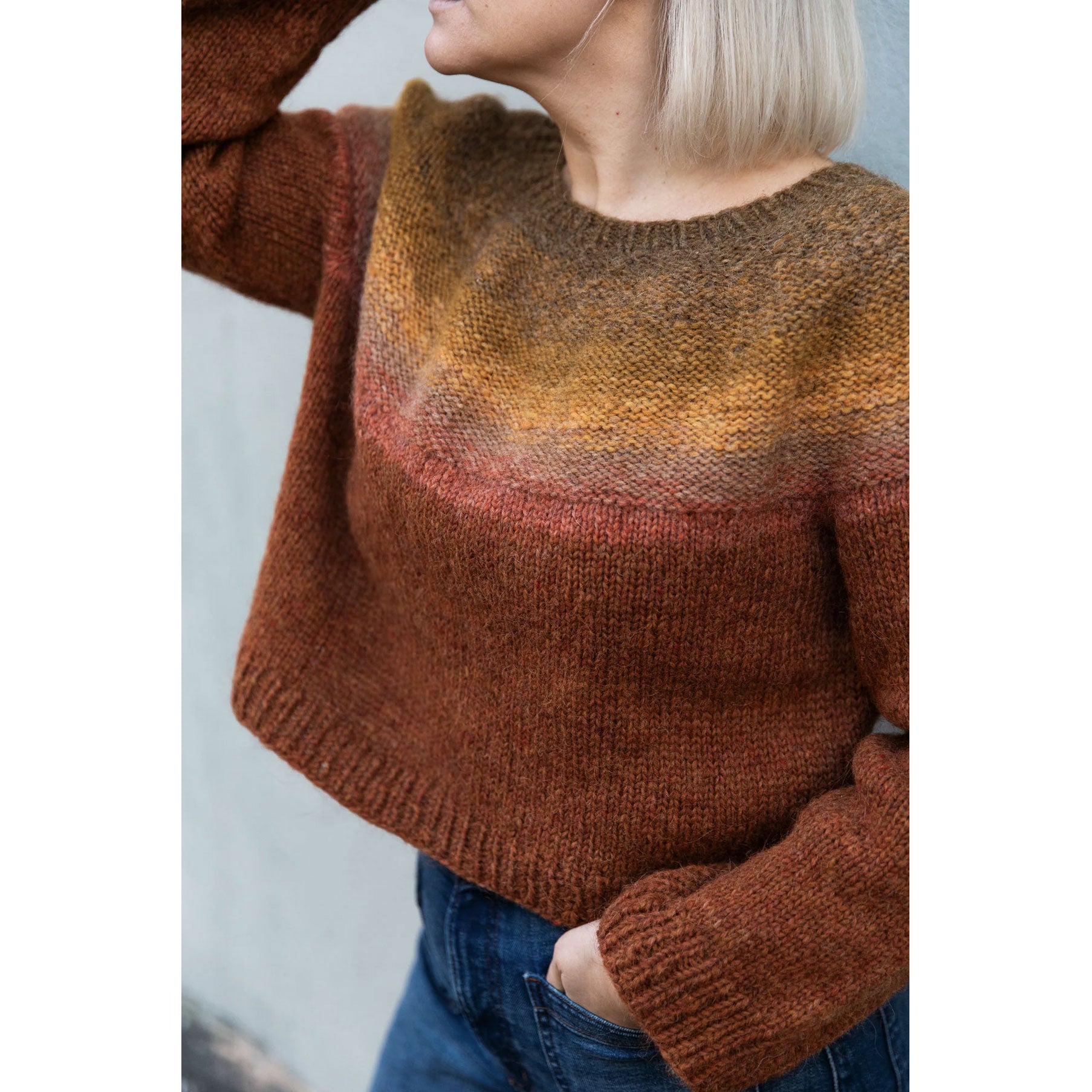 Person wearing a hand knitted brown gradient sweater against a light background