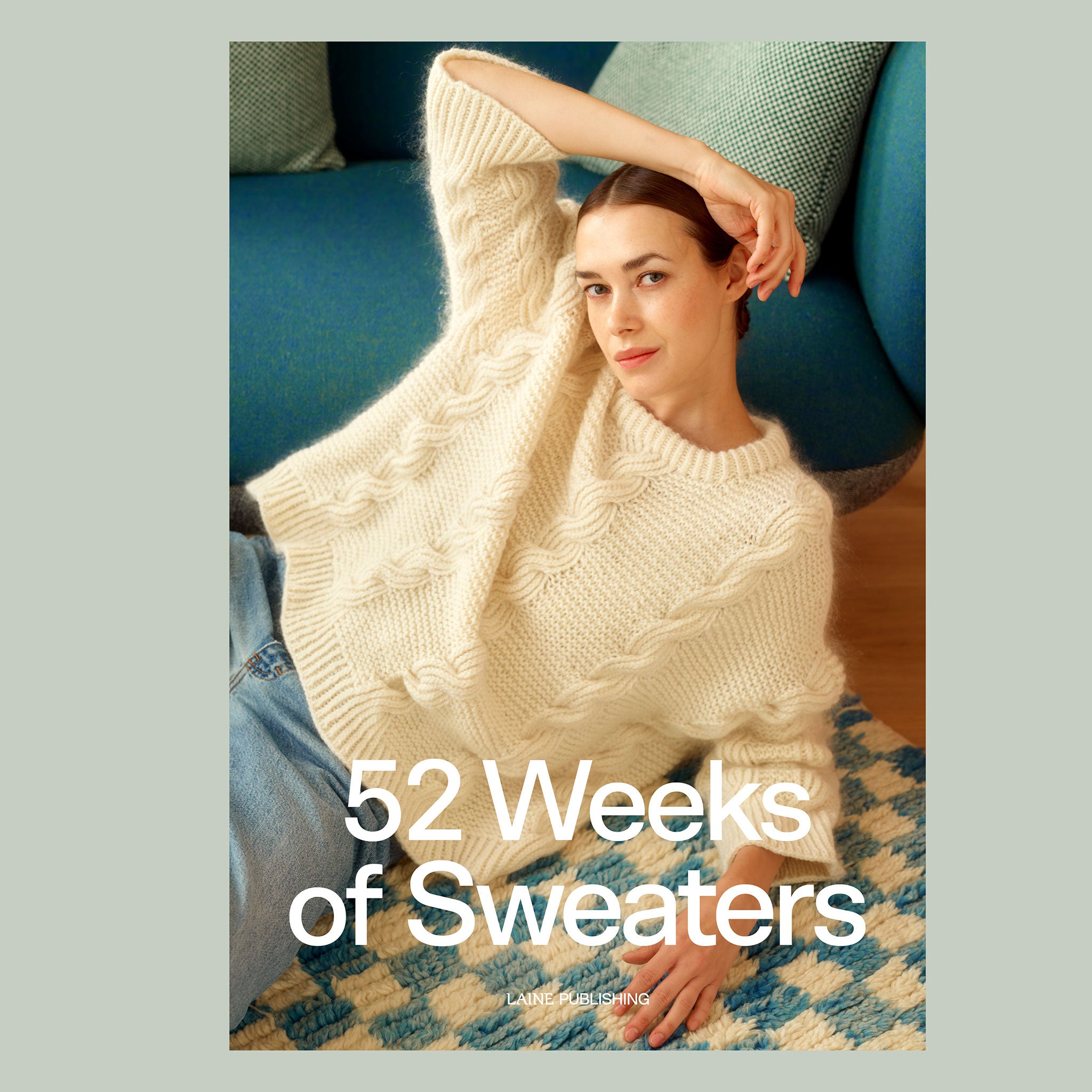 Cover image of ISBN9789527580738. Woman lying on blue and cream chequered pattern textured rug, wearing cream knitted garter stitch and cabled round neck sweater. 52 Weeks of Sweaters, Laine Publishing printed in white bold text across the bottom third of the image.