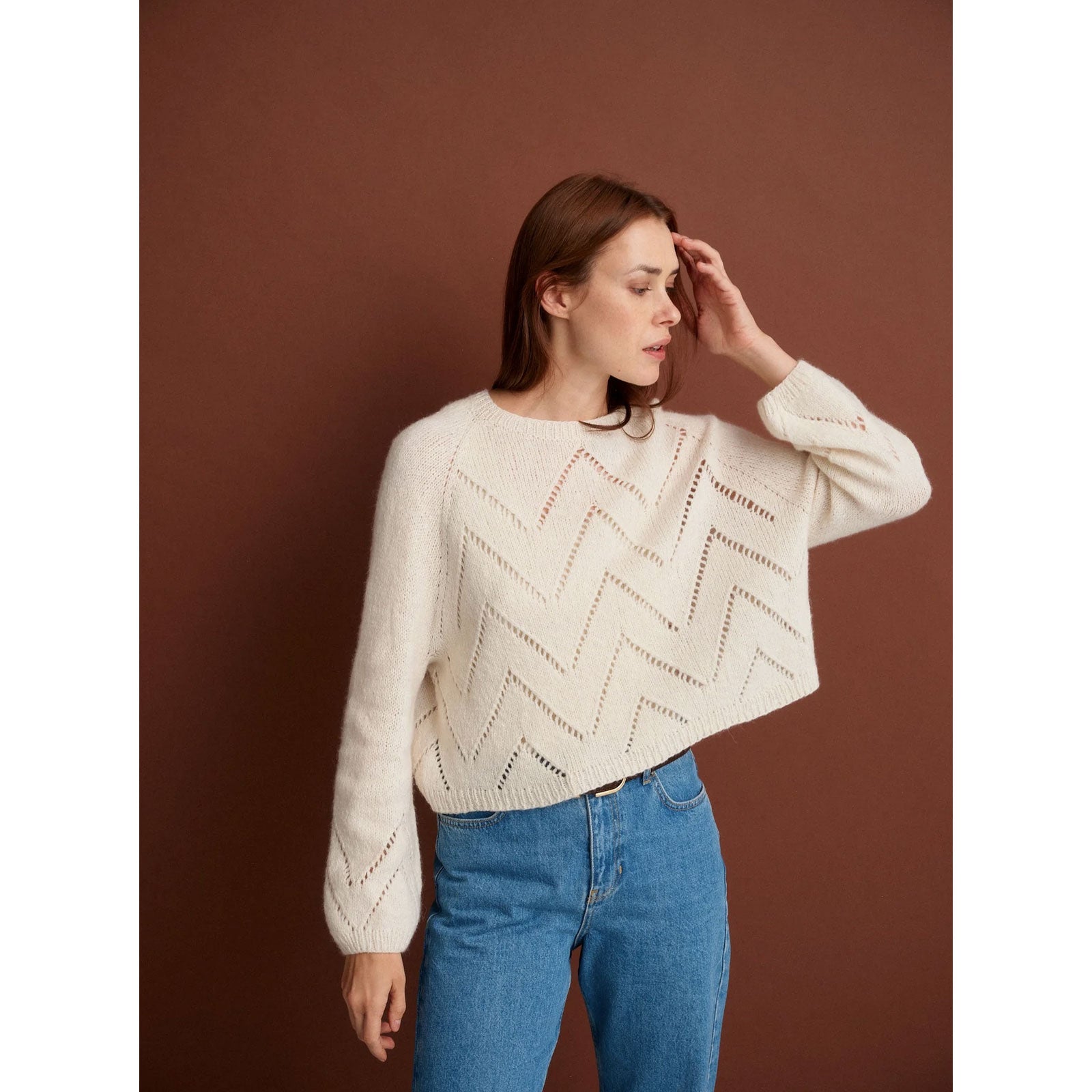 Woman wearing a cream sweater with a geometric pattern against a brown background