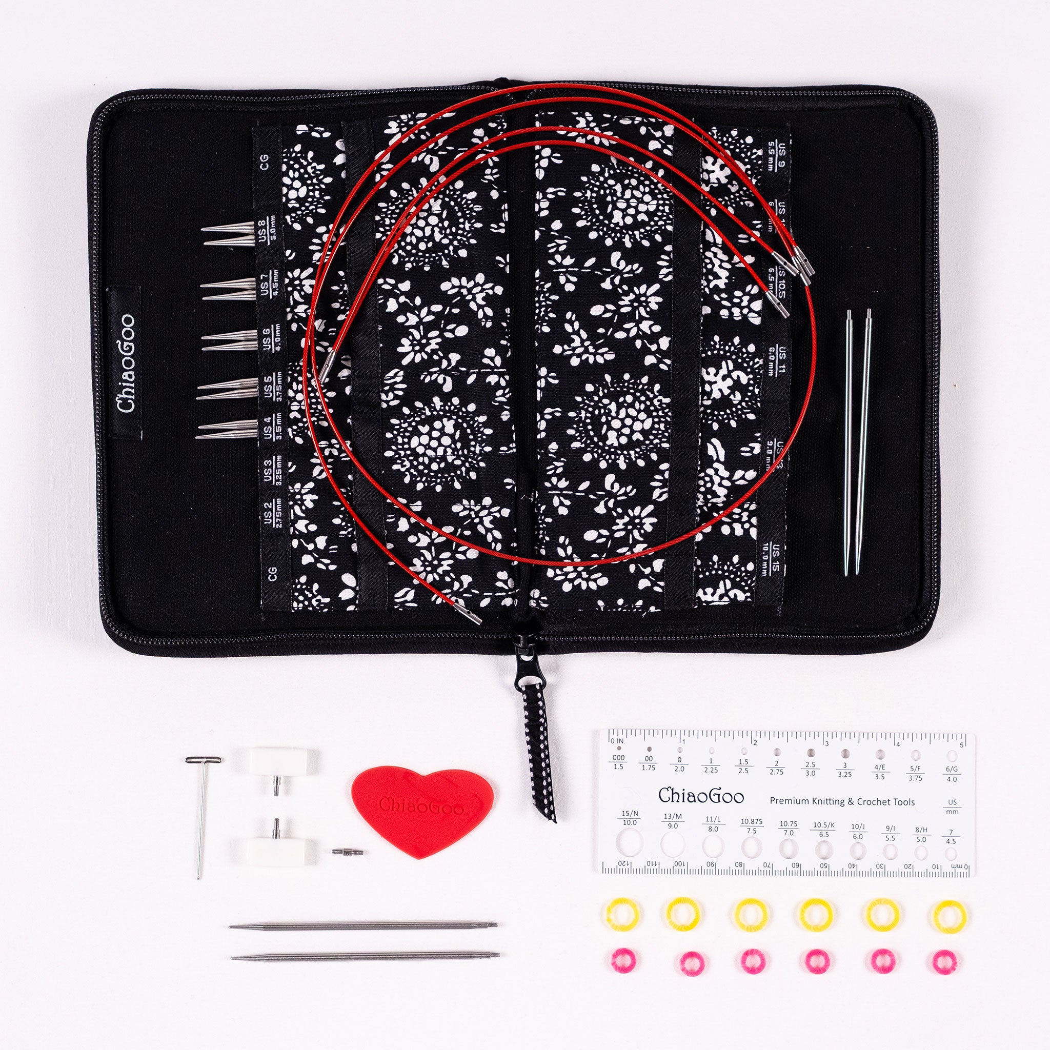 ChiaoGoo 4in Stainless Steel Interchangeable set showing black zippered storage case opened flat with labelled tip pockets, five pairs of tip in pockets, one pair of tips on case, four red lace cables, beneath display of tightening key, two small cable end stoppers, one small cable connector, one red heart rubber gripper, one pair of 2.75mm tips, white 5in plastic ruler gauge, six yellow and six pink stitch markers
