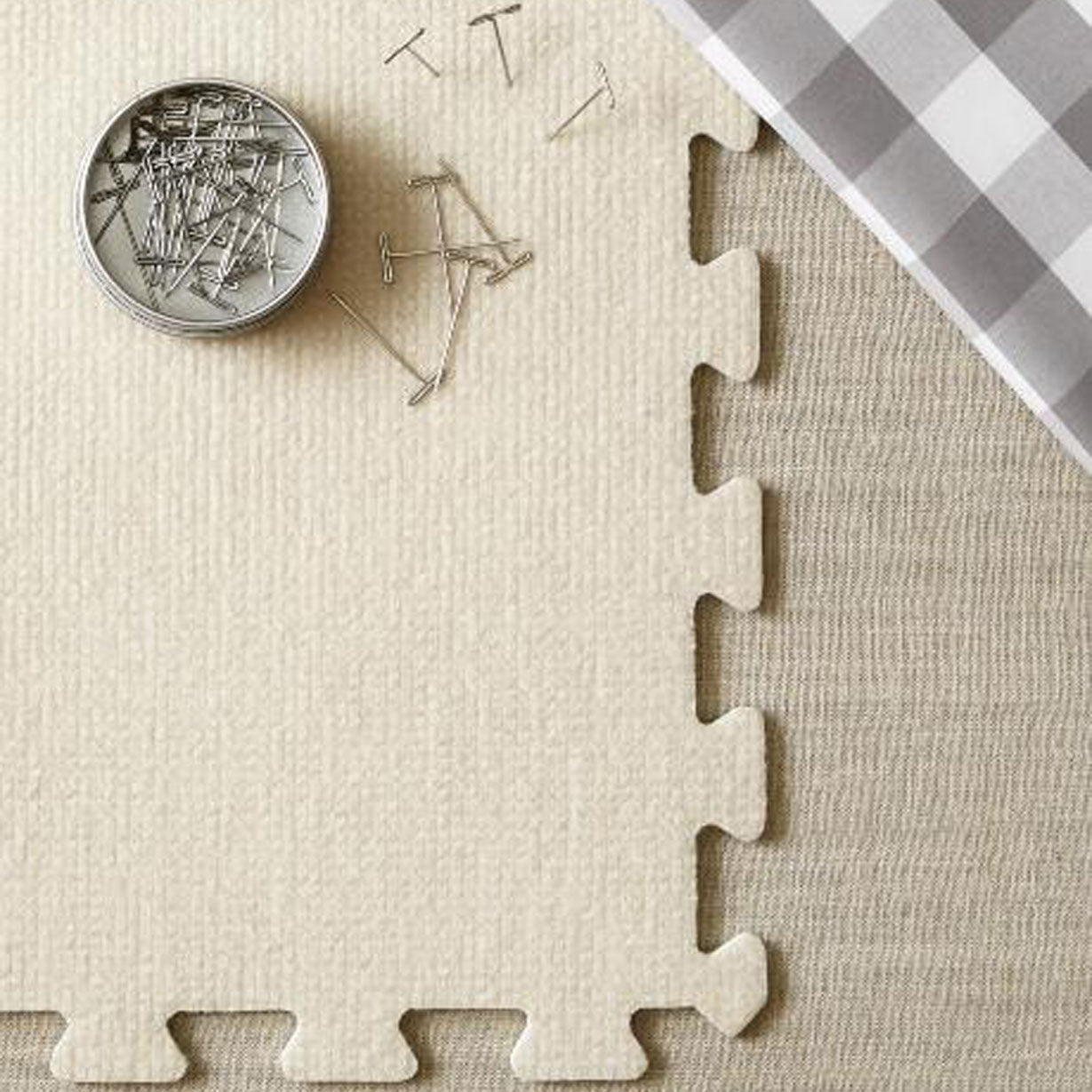 A close-up of a fibre covered EVA blcoking mat with T-pins pinned into the top corner and a section of gingham measuring cloth on a pale linen background