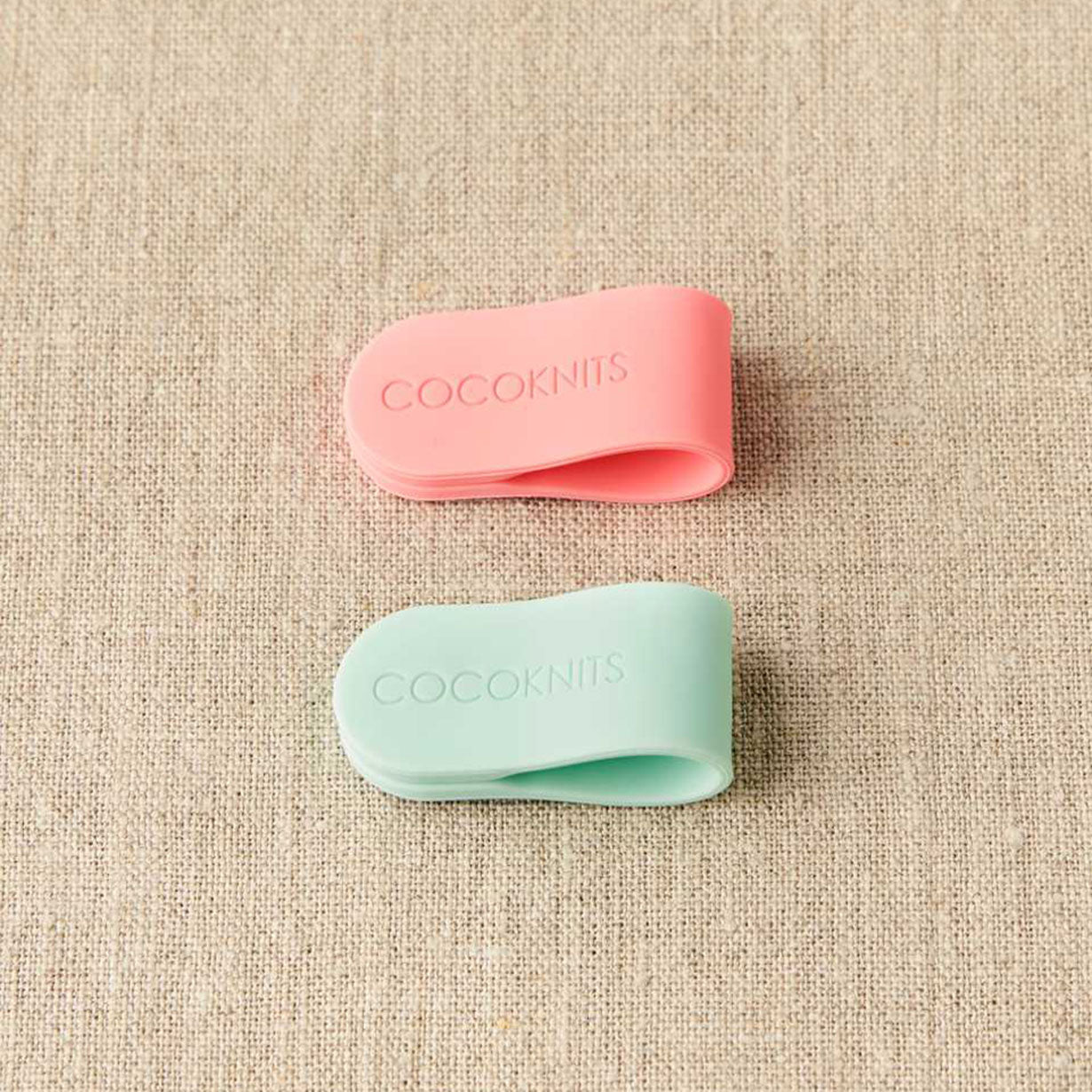 Cocoknits magnetic clips, one coral pink, one mint green on linen background