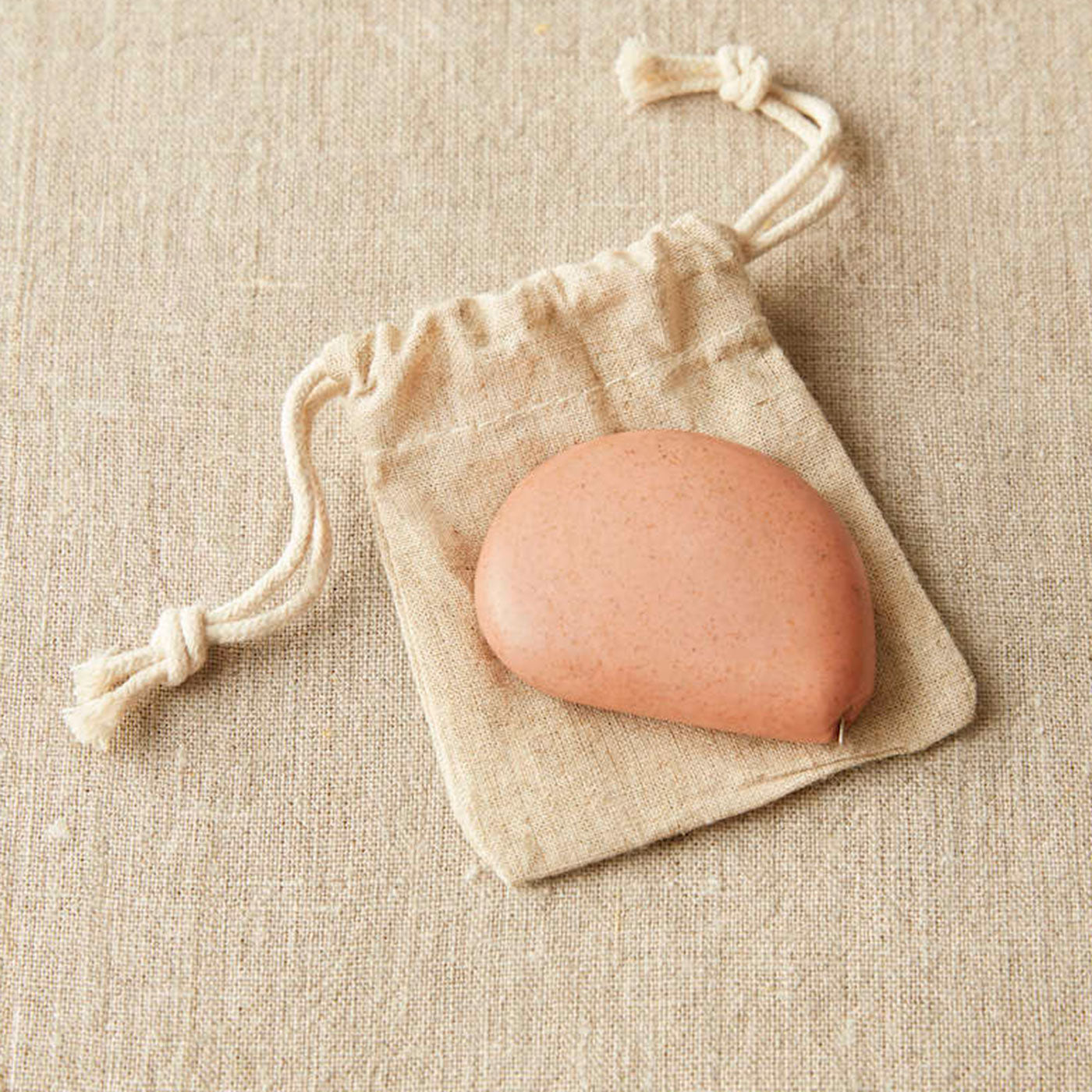 Terracotta coloured pebble shaped tape measure on linen drawstring bag