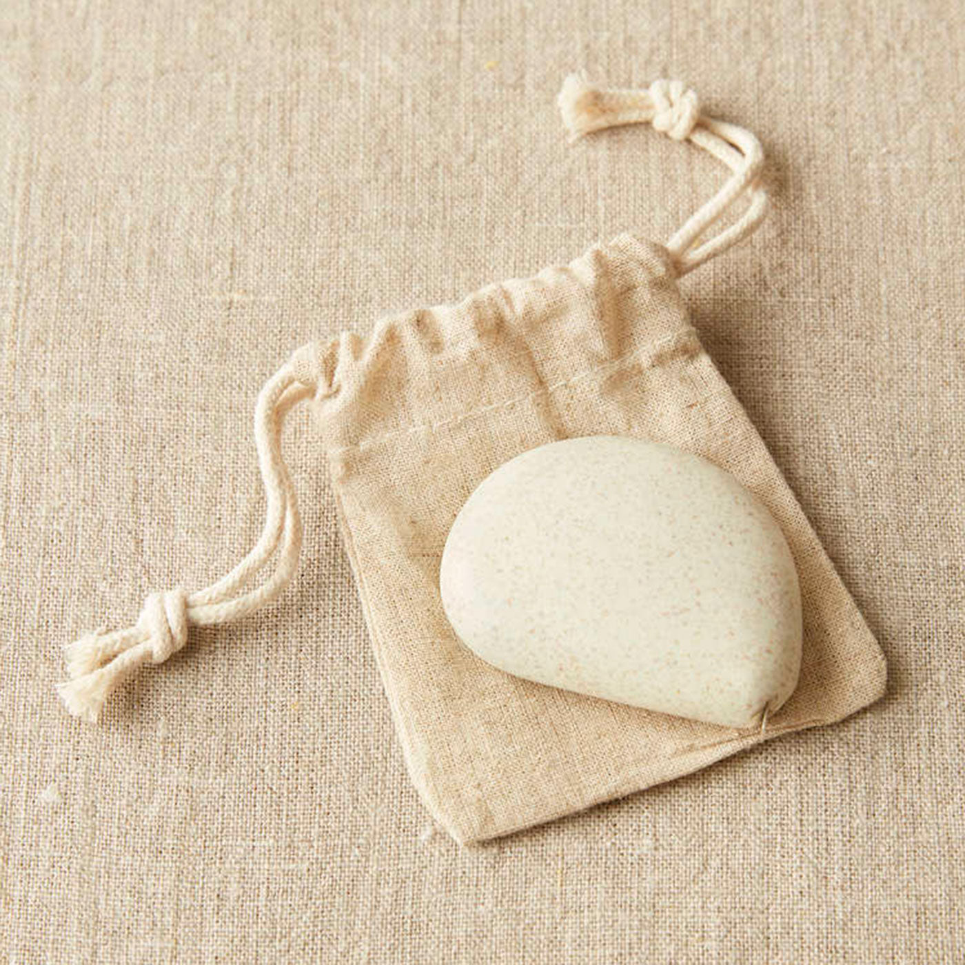 White coloured pebble shaped tape measure on linen drawstring bag