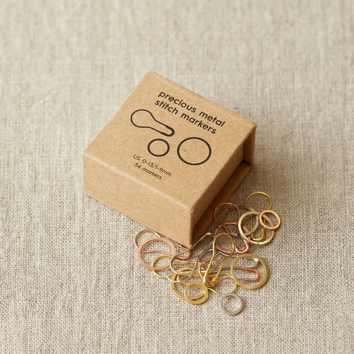 Box of Cocoknits precious metal stitch markers on a textured fabric background