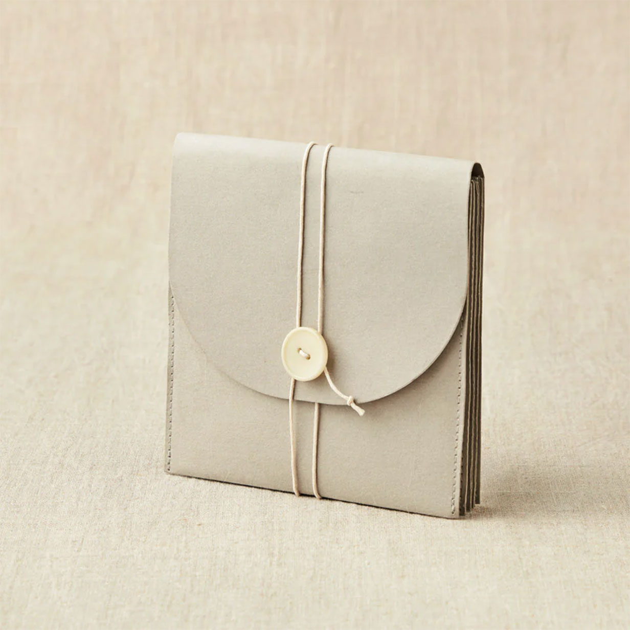 Cocoknits grey coloured paper based wallet closed with twine and button standing on linen background