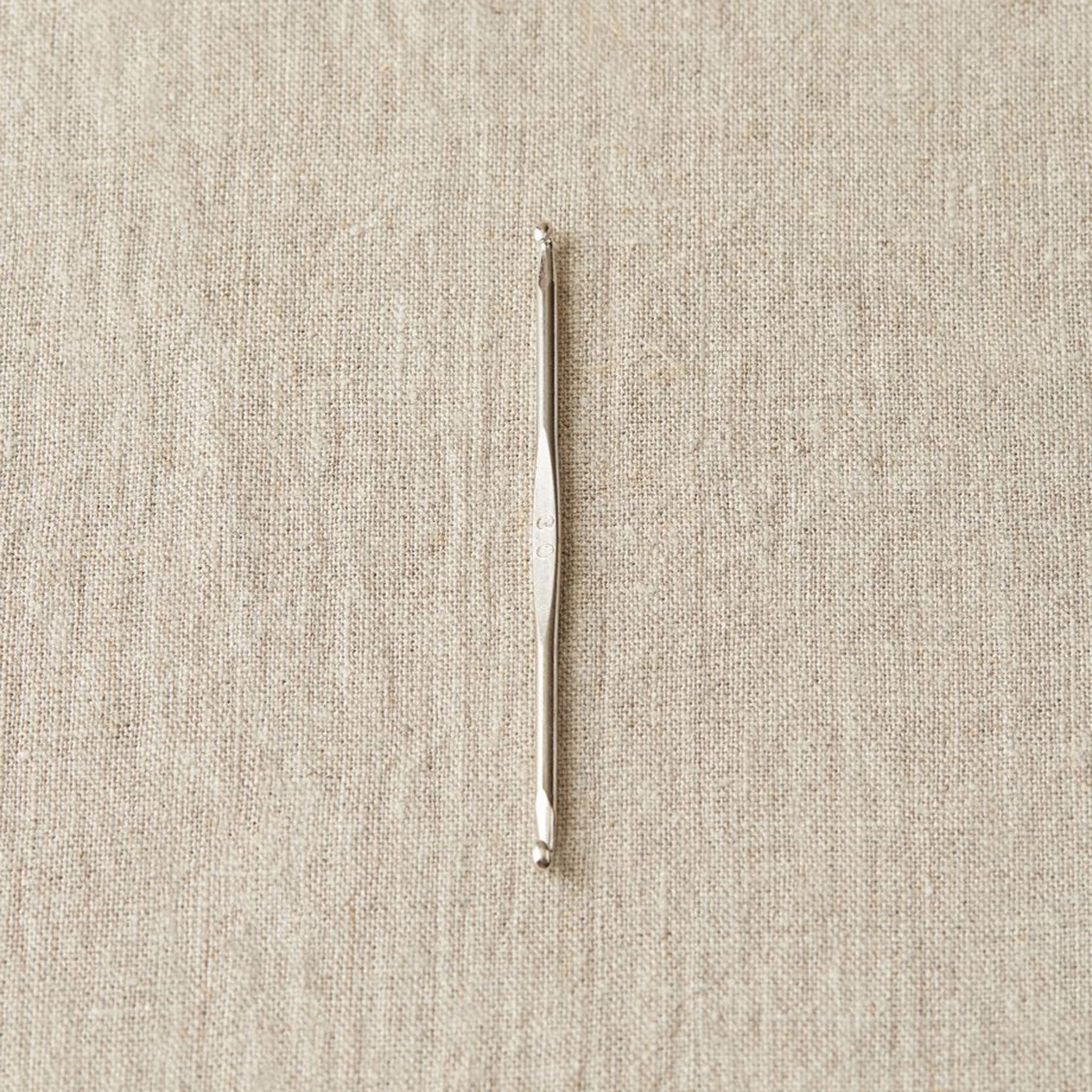 Stainless steel double ended crochet hook on a linen fabric for contrast