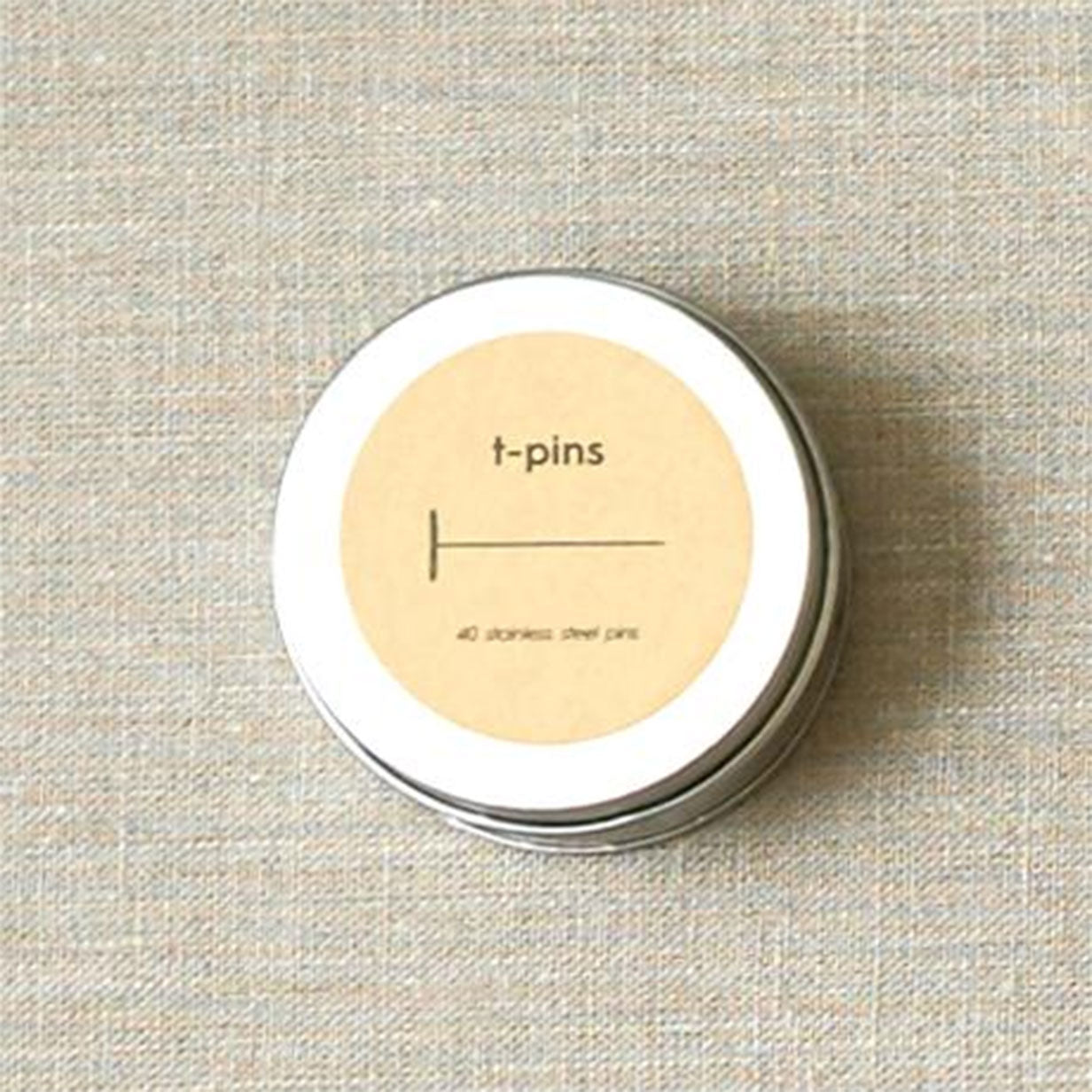Round tin labelled t-pins shown on linen fabric surface