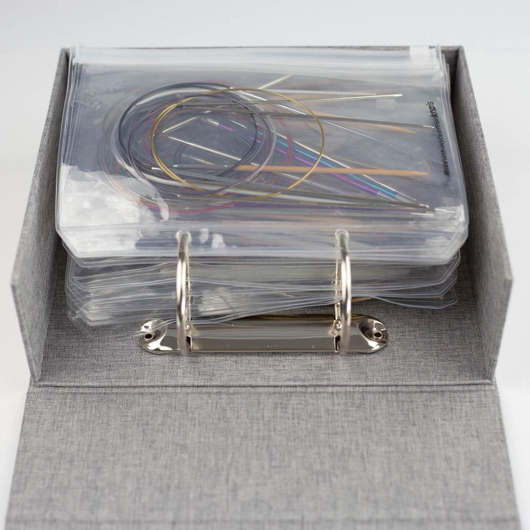 Side view of Knools grey needle garage ring binder folder with clear plastic pockets holding various styles of fixed circular knitting needles 