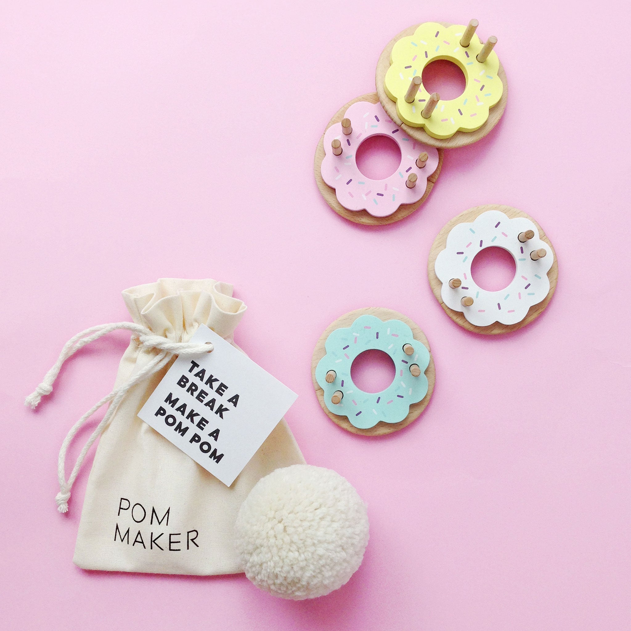 Pom pom maker with colorful donut-shaped pom poms on a pink background