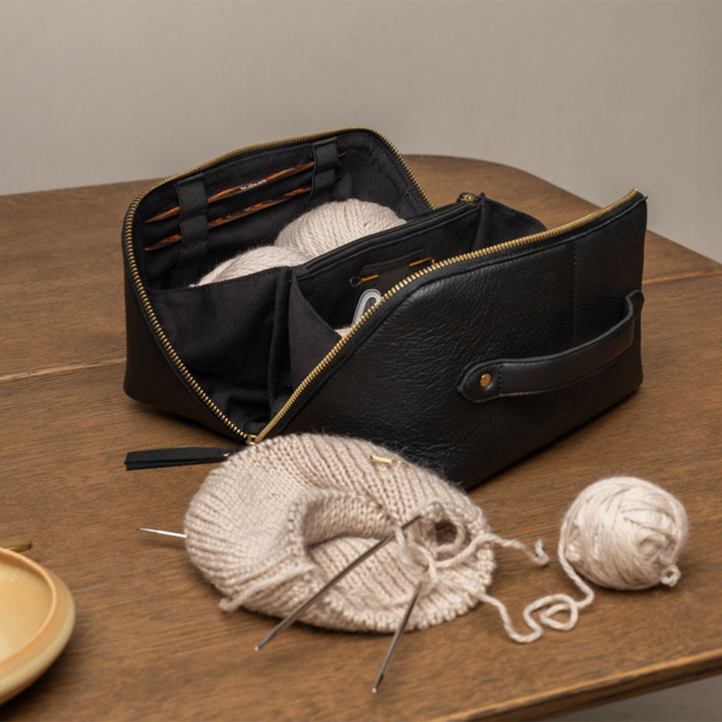 Black leather knitting bag with yarn and needles on a wooden surface