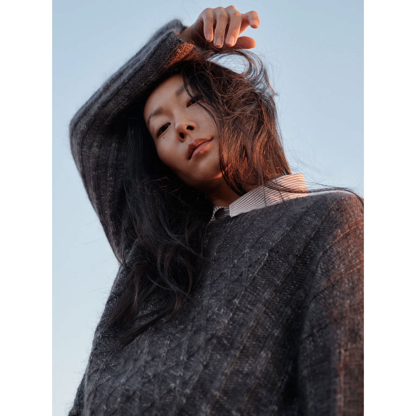 Woman wearing a dark knit hat and sweater against a light blue sky.
