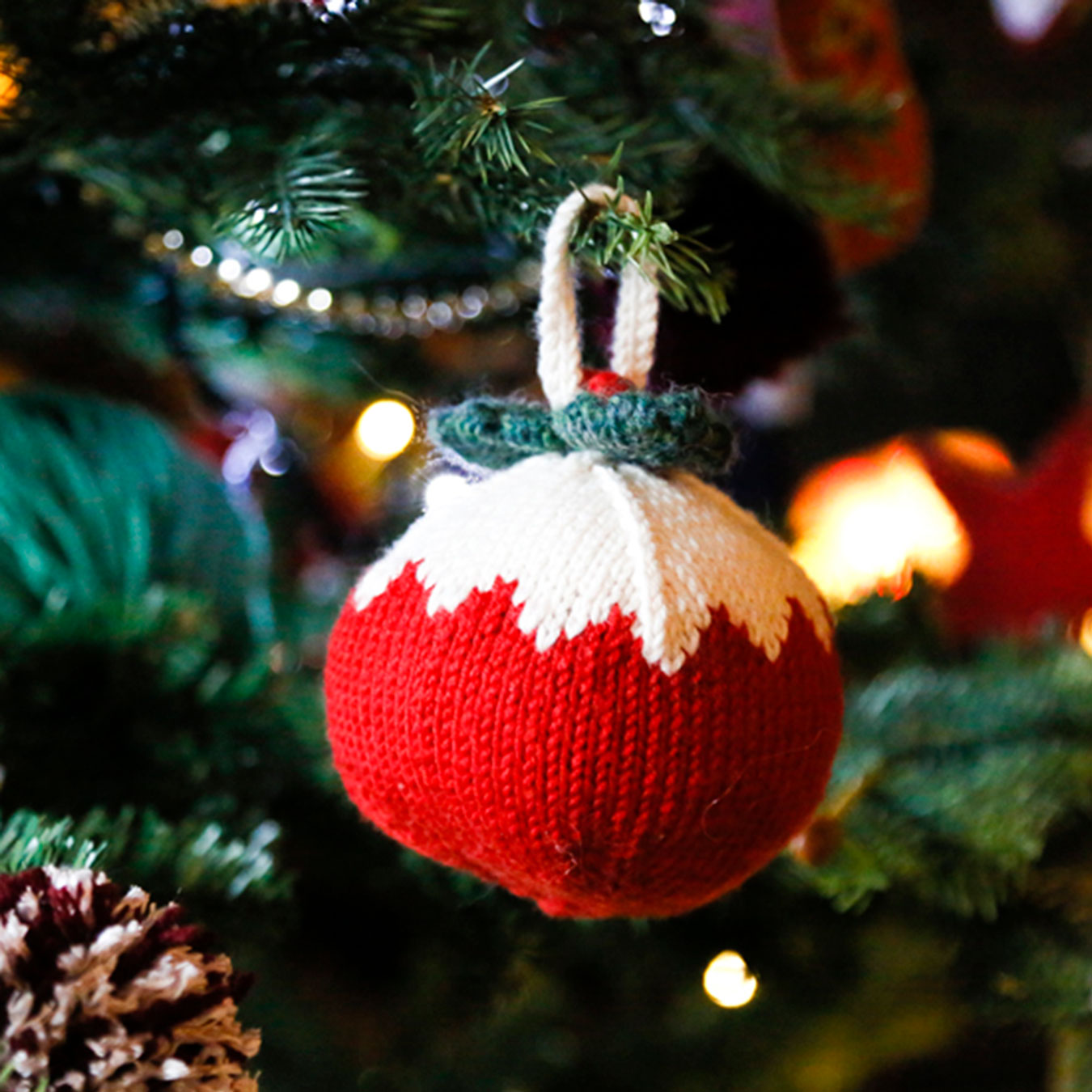 Knitted Christmas ornament on a tree with blurred lights in the background