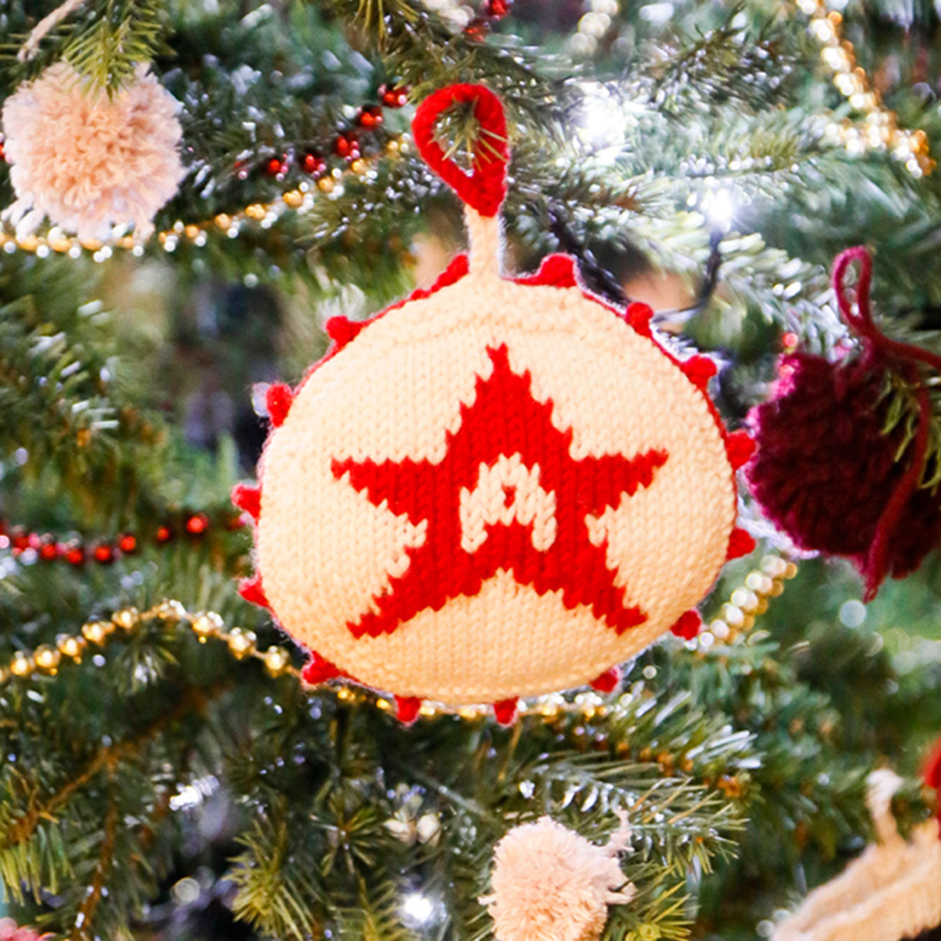 Knitted Christmas ornament with red star design hanging on a tree.